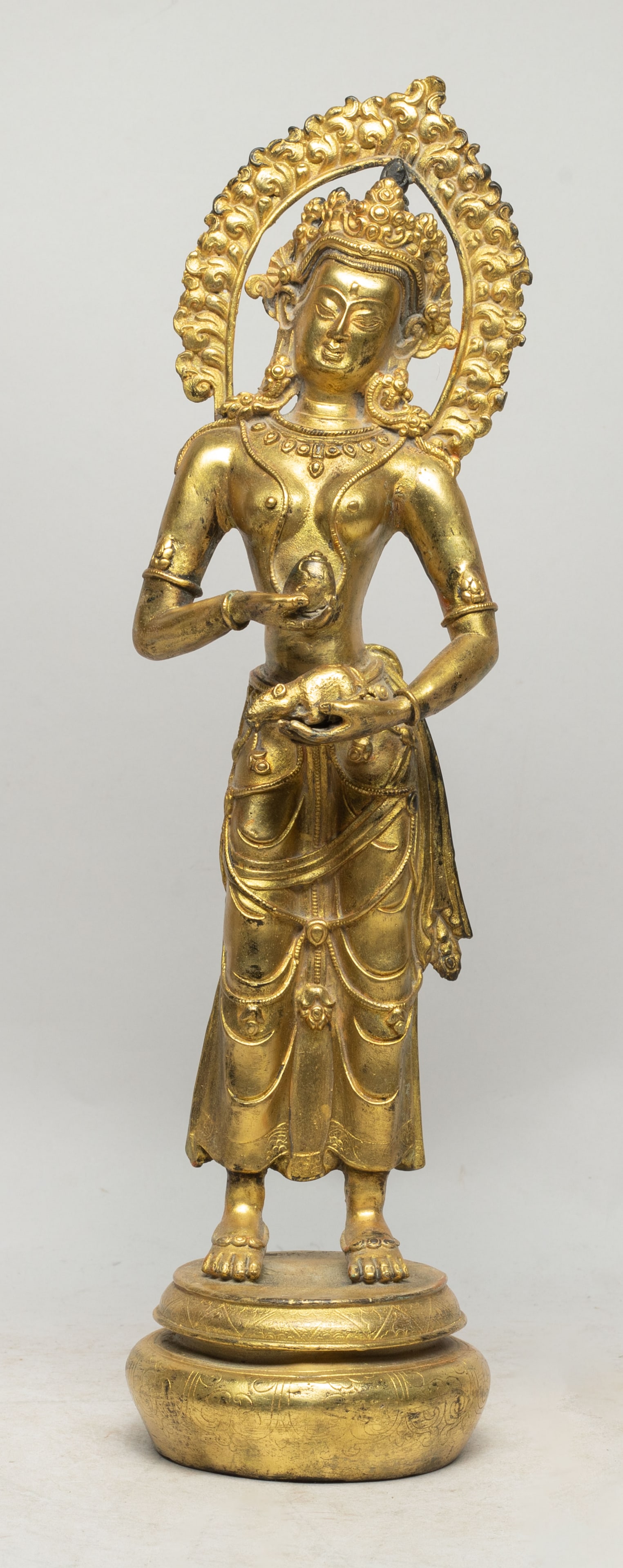 Tall Chinese Gilt Bronze Sculpture of Buddha: Tall Chinese gilt bronze Buddha, cast standing on a rounded base, the left hand holding a mouse and right hand holding an implement, wearing an elaborate diadema, the bottom incised with a Buddhist sy