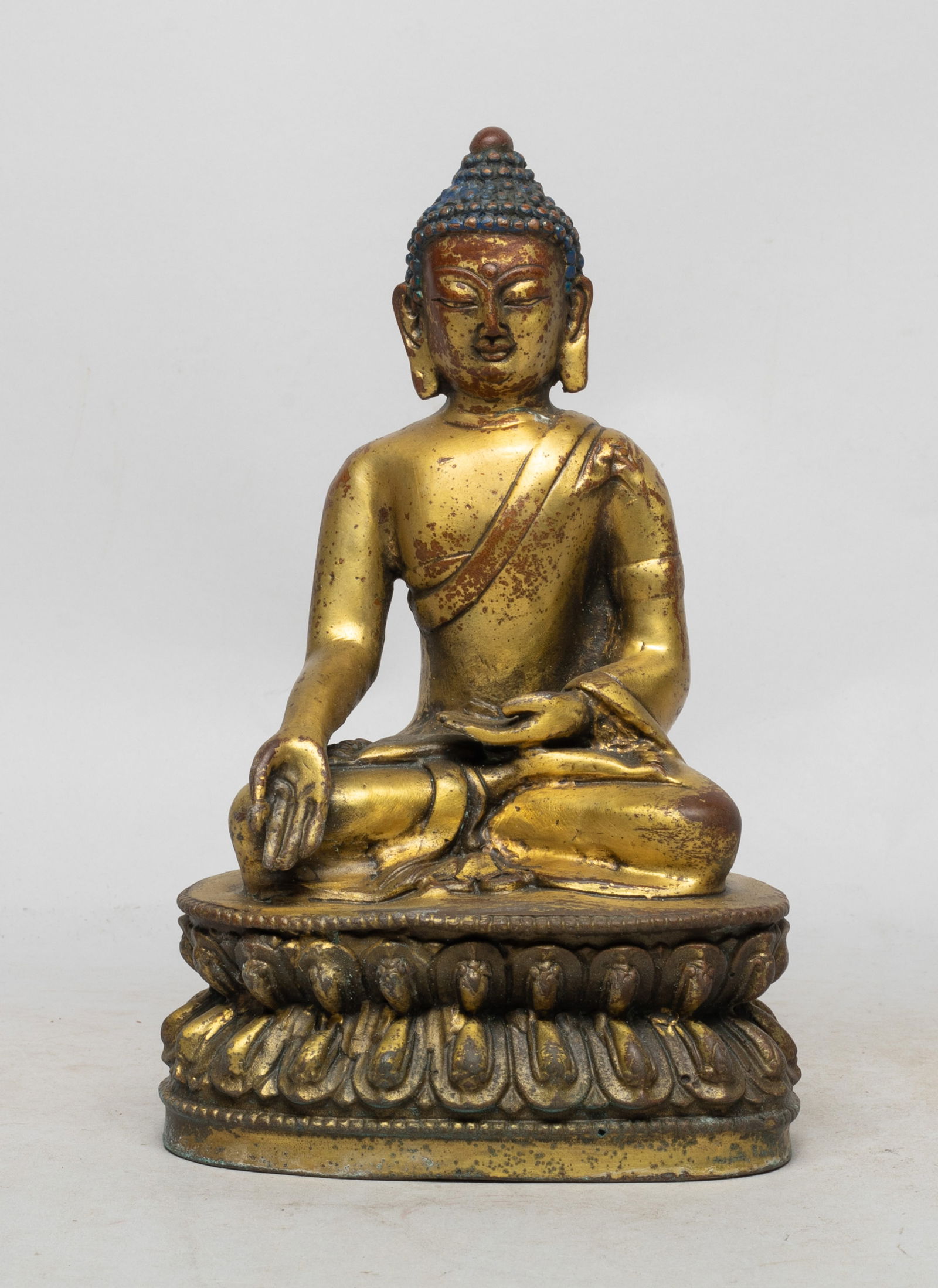Estate Chinese Gilt Bronze Buddha: The Buddha cast seated on a waisted lotus throne, the left hand in abhaya mudra and right hand in vitarka mudra, the rounded face surmounted by raised hair coils and flanked by a pair of pendulous ear