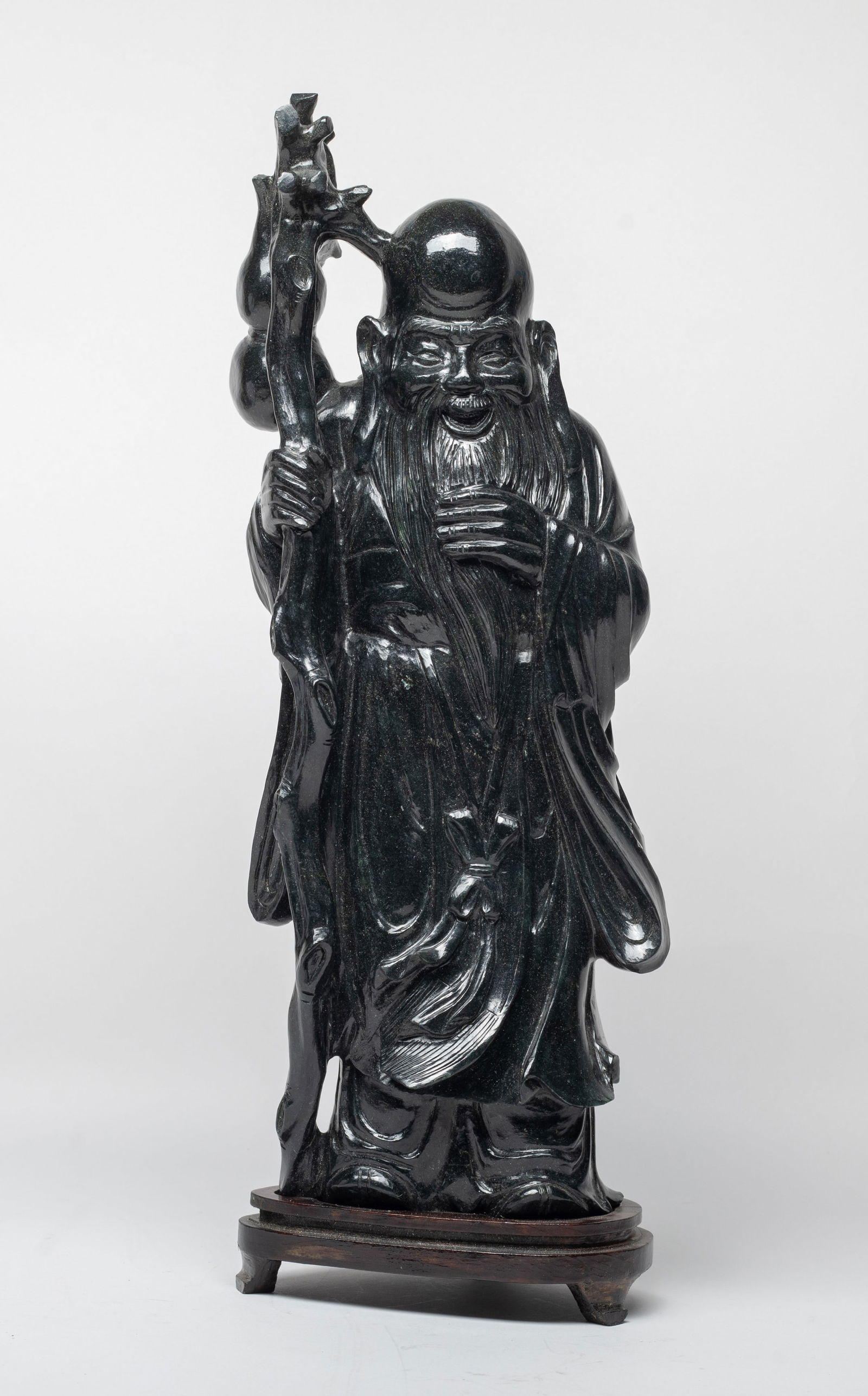Tall Vintage Chinese Spinach Jade Sculpture: The Shoulao gracefully carved standing with his left hand smoothing beard and right hand holding a tall gnarled stick suspended with a gourd, with stand. Approx. 16*5.5*3.7 inch (w/ stand).