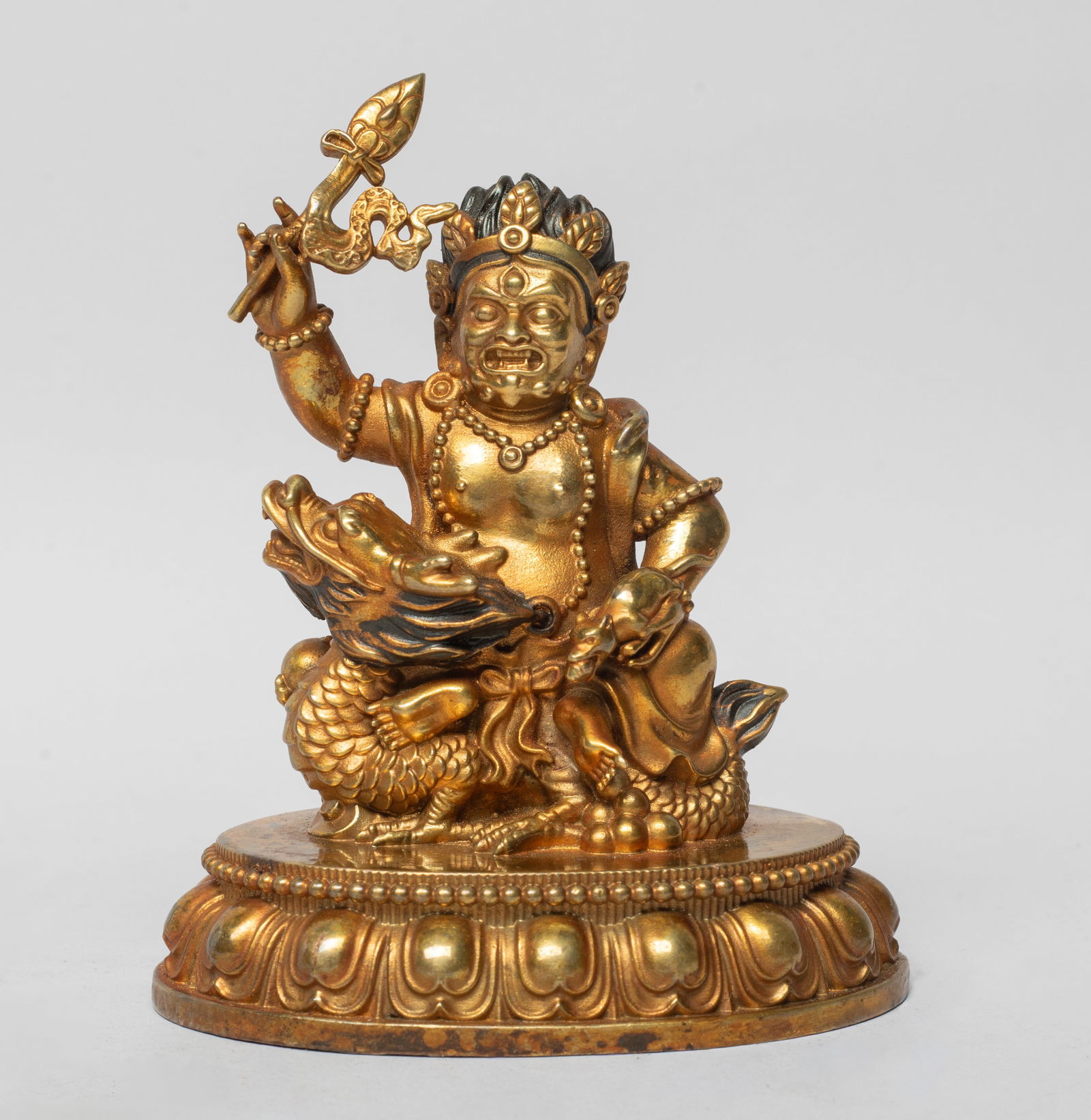 Chinese Gilt Bronze Sculpture of Buddha: The Buddha cast seated on a ferocious dragon on a lotus base, the left hand grasping a mouse and right hand holding an implement, wearing beaded jewelry and a leaf crown. Approx. 3.9*3.3*2.4 inch.
