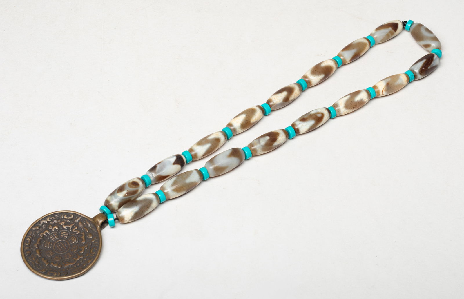 Chinese/Sino-Tibetan Dzi Bead Necklace: Chinese / Sino-Tibetan dzi bead necklace, spaced by disc beads, suspended with a metal pendant cast with traditional motif. Approx. 20inch L.