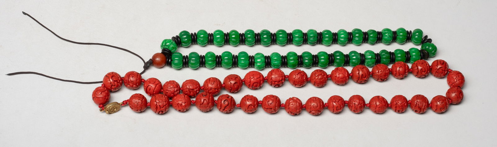 Chinese Cinnabar & Stone Necklace: Including a necklace of green stone beads carved of pumpkin form, spaced by disc beads, and a necklace of cinnabar beads carved with flowers. Approx. 23 inch L (longer necklace size).
