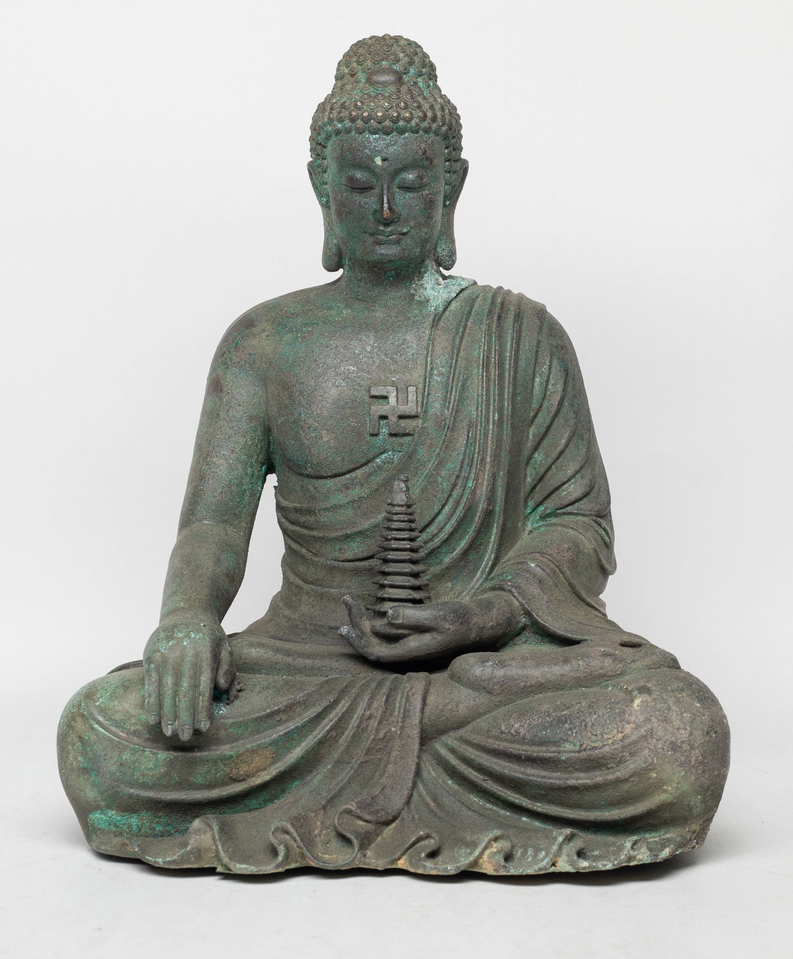 Estate Chinese Bronze Cabinet Sculpture of Buddha: The Buddha cast seated in dhyanasana, the left hand holding a pagoda and right hand resting on knee, wearing a loose-fitting robe open at the left shoulder and chest revealing a swastika symbol, the f