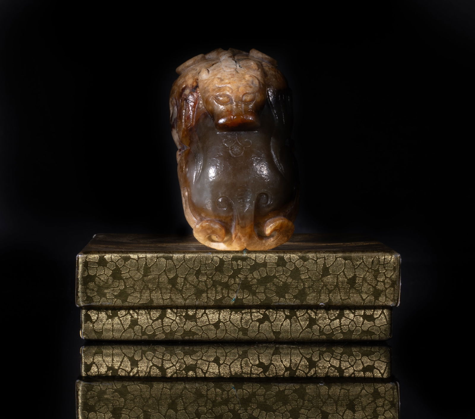 Rare Chinese Russet Jade Beast Sculpture: The recumbent beast deftly carved in the round, its head turning inwards towards its back, detailed in relief with a bifurcated horn and a bifurcated tail, the muscles of the body accentuated by