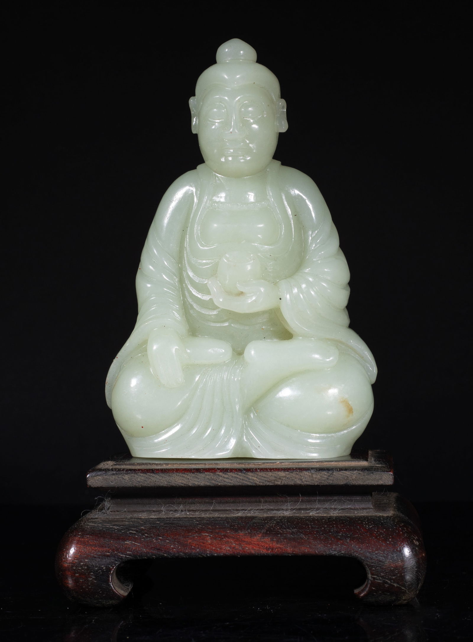 Estate Chinese Jade Buddha on Wood Base: The jade Buddha carved seated in dhyanasana, the left hand holding an elm bowl and right hand resting on knee, wearing a long and loose robe, the rounded face with serene expression, wood stand. Appro