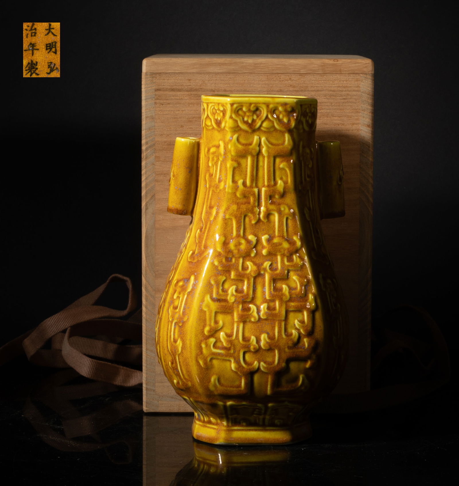 Chinese Export Yellow Glazed Porcelain Vase: The faceted body raised on a gently spreading foot, flanked by two tubular handles, the exterior carved with stylized dragons, overall covered in a variegated yellow and brown glaze suffused with
