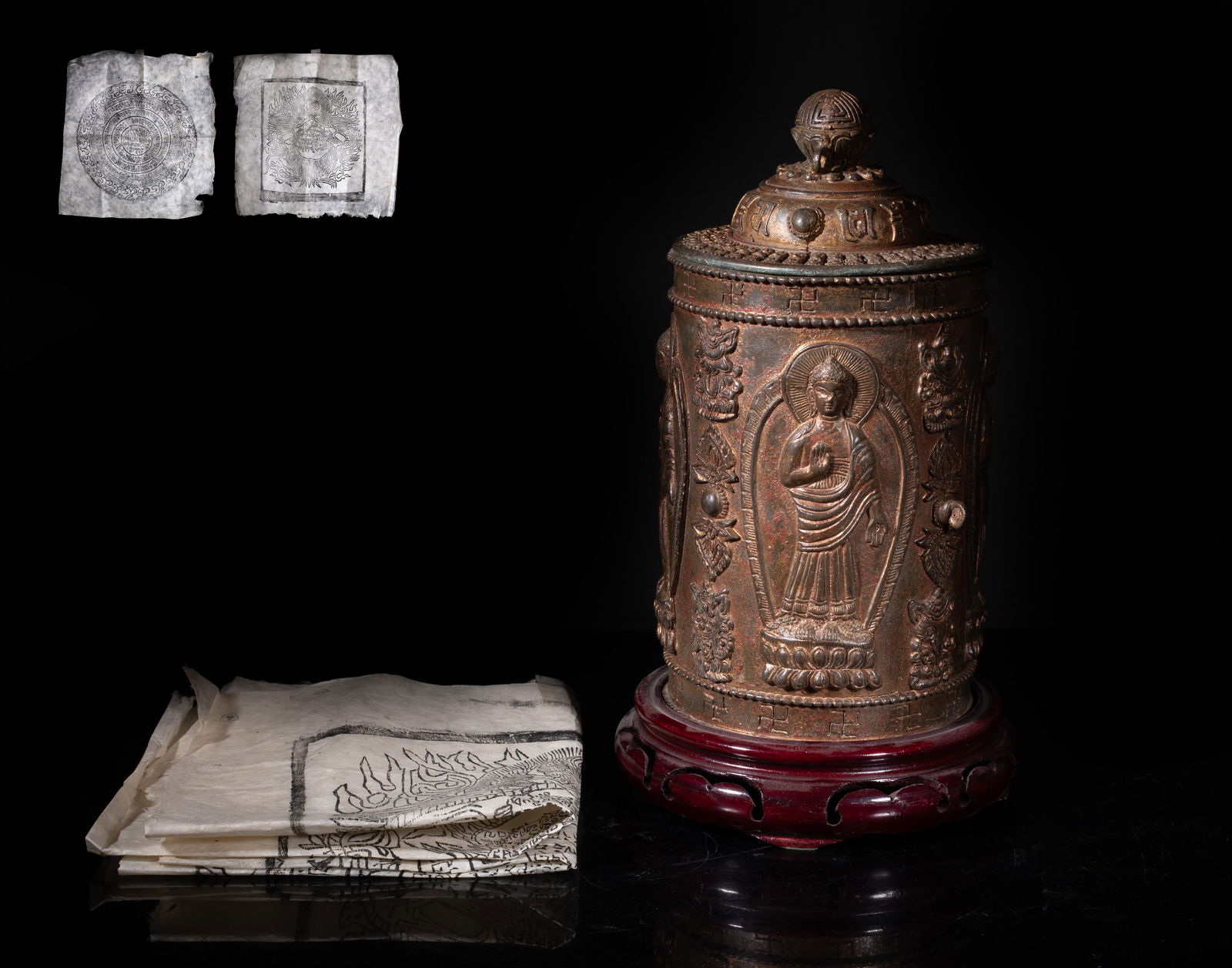 Tall Chinese/ Tibetan Bronze Scriptures Jar: Of cylindrical form the exterior cast with four Buddha standing on lotus base, separated by Buddhist treasures, below a band of swastika symbols, the cover with a globular knob surrounded by bands of