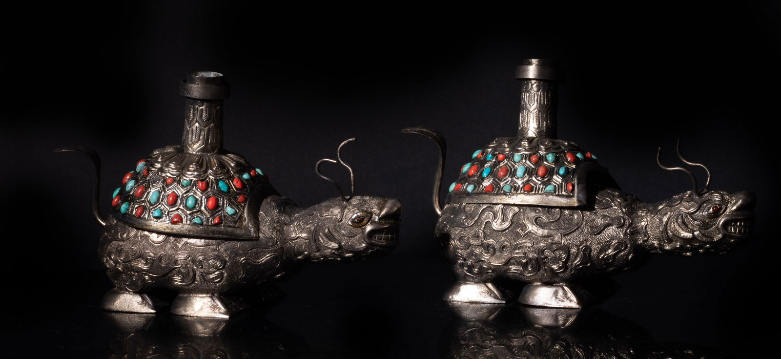 Estate Two Chinese Silver Tone Candlesticks: Two Chinese silver tone candlestick holders, molded of mythical beast form, the body cast with stylized birds and beasts amongst clouds, the shell inlaid with stone and supported the holder. Approx. 7