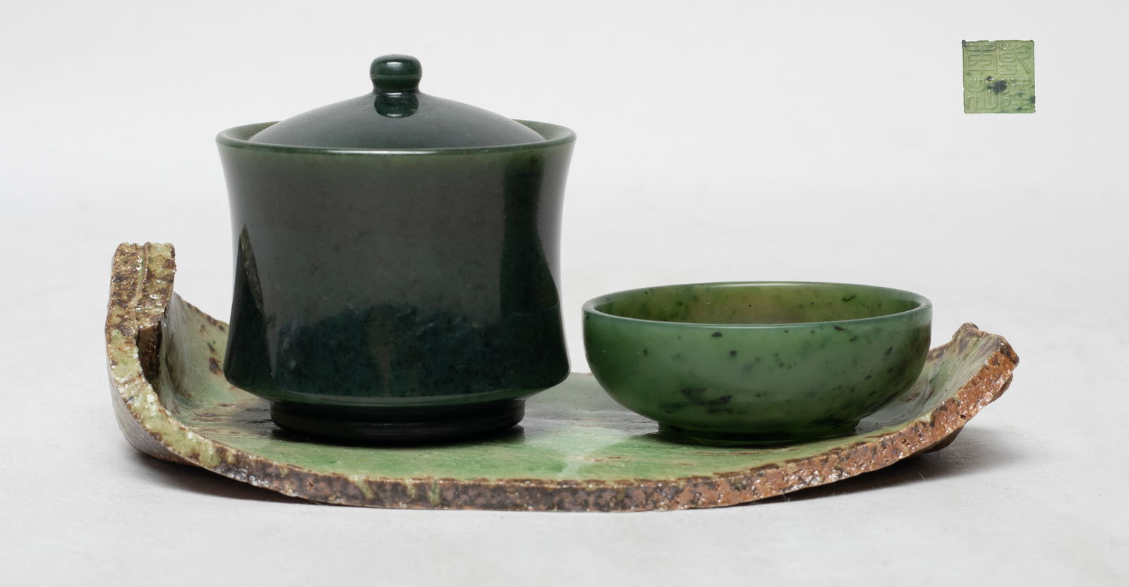 Chinese Spinach Jade Cups w/ Porcelain Base: Two Chinese spinach jade carved cups, the larger cup with a lid, accompanied with a leaf form porcelain base. Approx. 2.07*2.13 inch (larger cup).