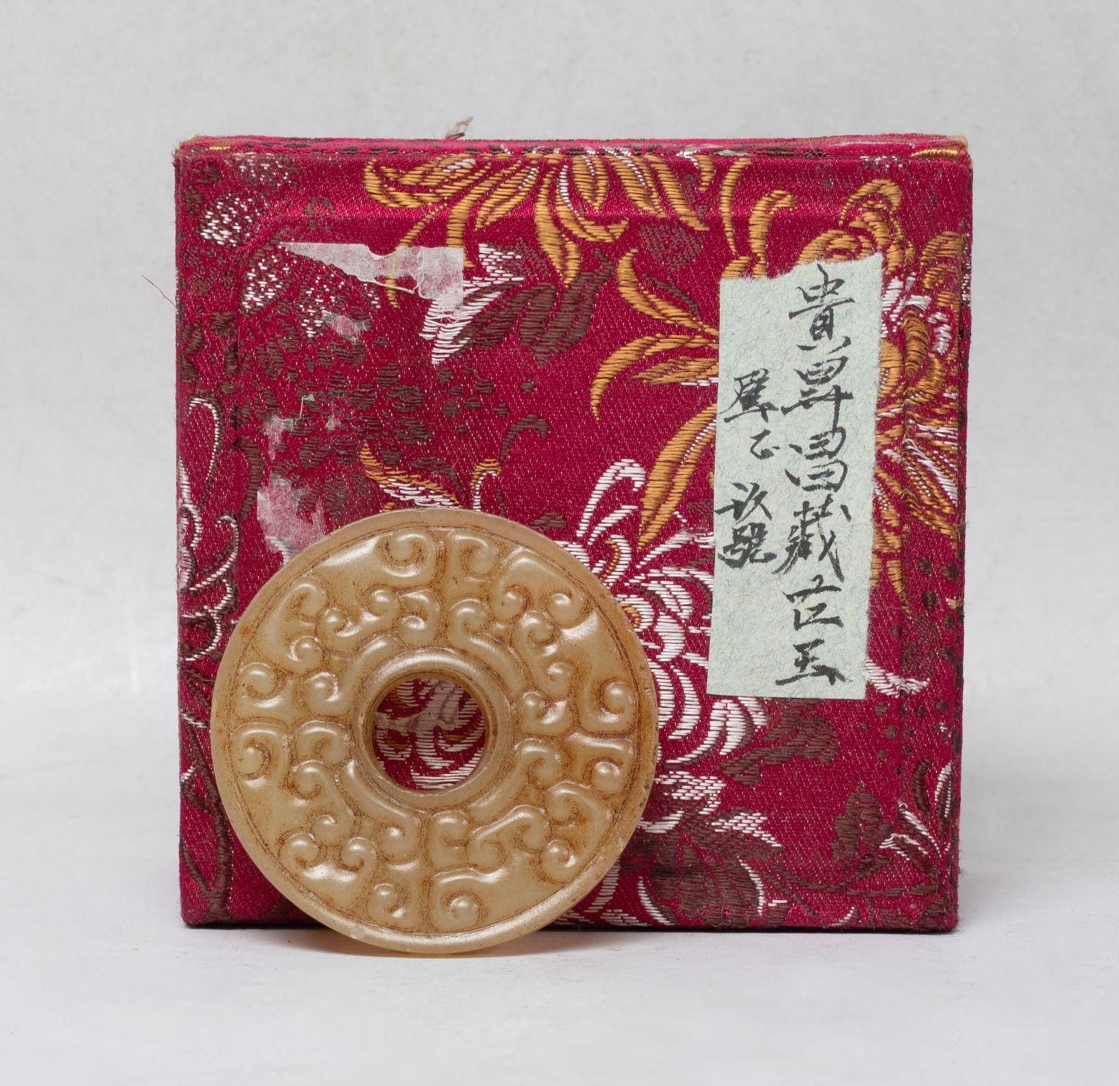 Chinese Export Jade Pendant of Bi: Of circular shape, pierced with an aperture at the centre, either side carved in raised relief with archaistic scrolls, with box. Approx. 2.07 inch D (w/o box).