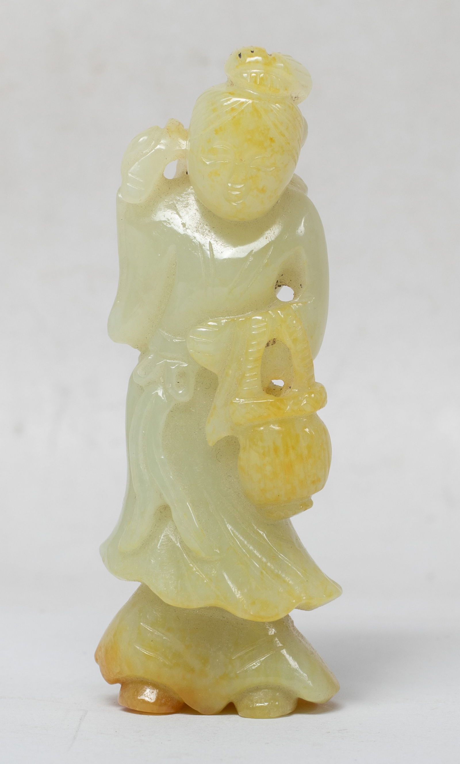 Estate Chinese Russet Jade Figure: Chinese russet jade toggle, carved as a standing lady dressed in a long flowing robe, carrying a basket on left arm and right hand grasping flower stem. Approx. 3.2*1.05*0.75 inch.