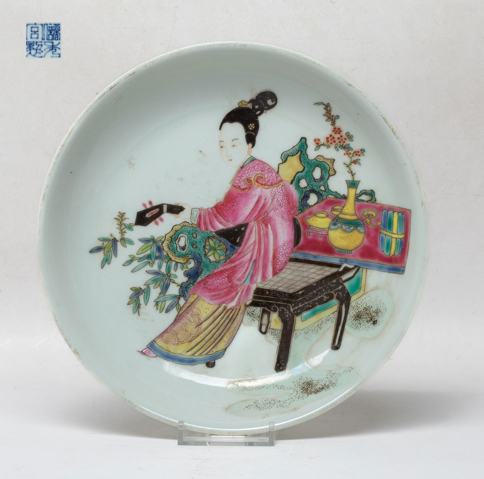 Chinese Famille Rose Porcelain Plate: The plate interior painted with a lady sitting around a table and rockery, playing with an instrument in hands, the bottom with a four-character mark. Approx. 8 inch D.