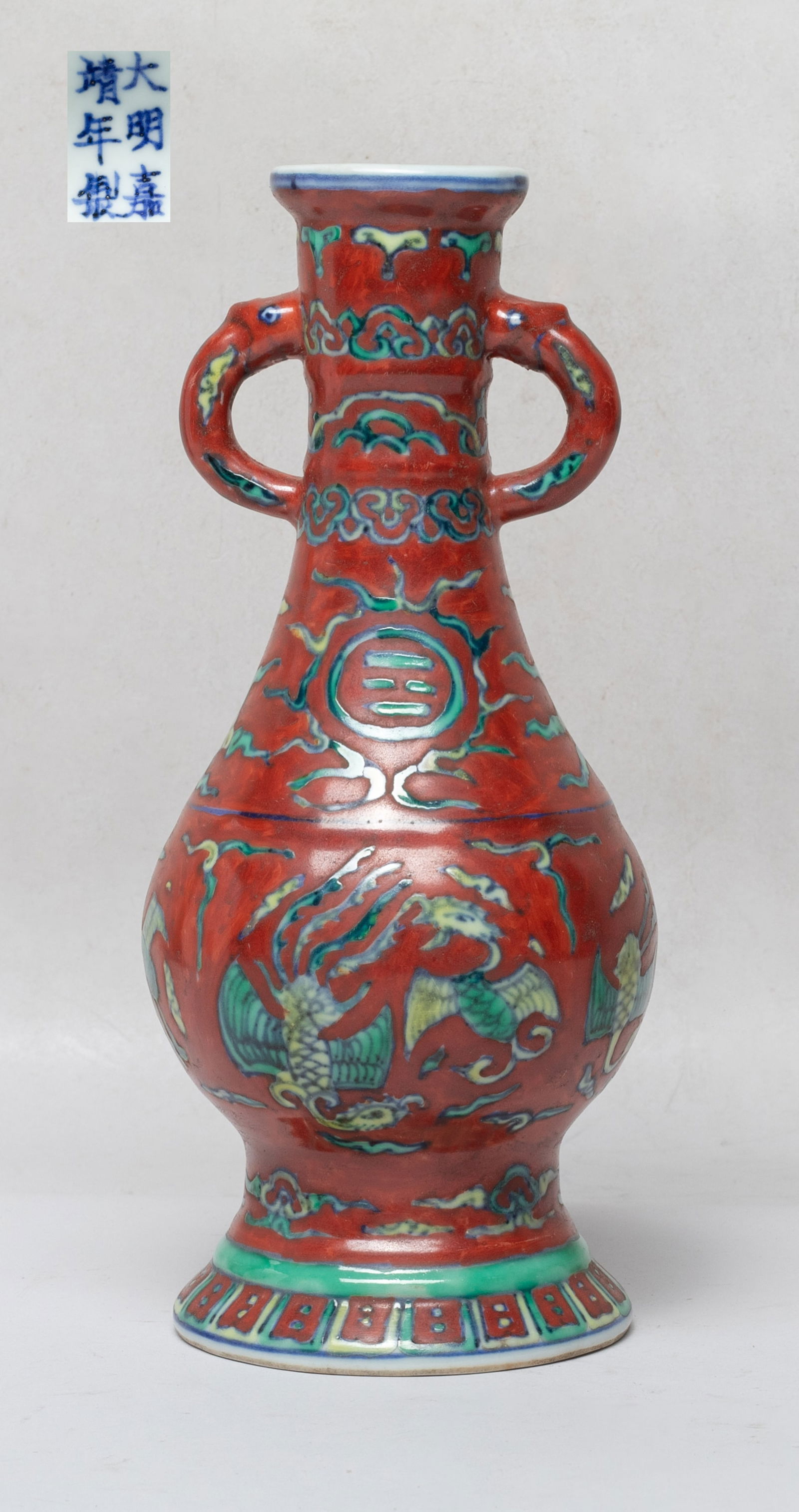 Chinese Export Porcelain Cabinet Vase: Of pear shape rising from a splayed foot to a columnar neck, flanked by two stylized handles, the exterior painted with phoenixes, traditional symbols and clouds on red glazed ground, the bottom