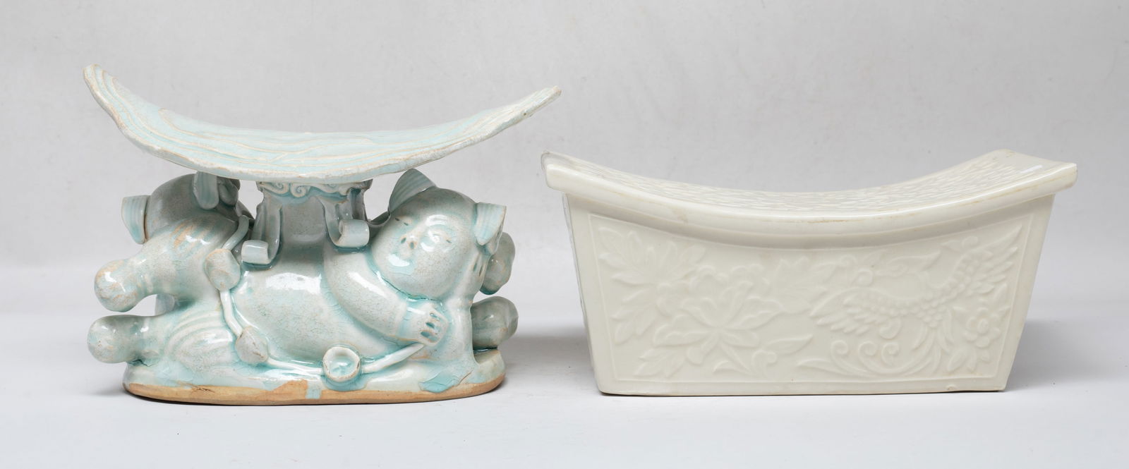 Two Chinese Export Porcelain Pillows: One pillow carved in low relief with phoenix and peony foliage, overall covered with creamy glaze, the other molded as two boys lying back to back, supporting a large lotus leaf form top, applied