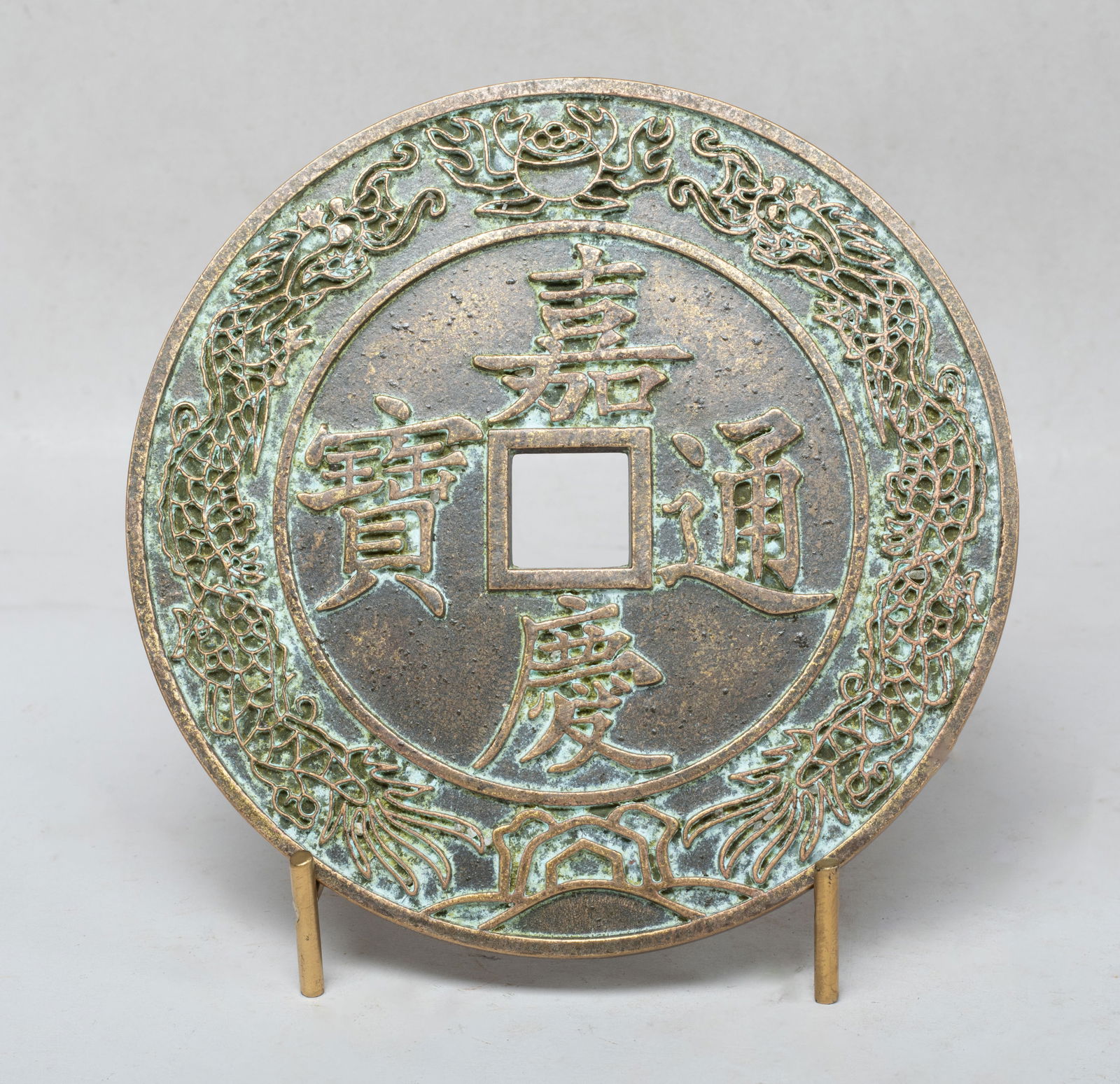 Large Chinese Export Bronze Coin Type Sculpture: Large Chinese bronze coin form sculpture, either side cast with a pair of dragons pursuing a flaming pearl, framing central four characters, with stand. Approx. 5.8 inch D (w/o stand).