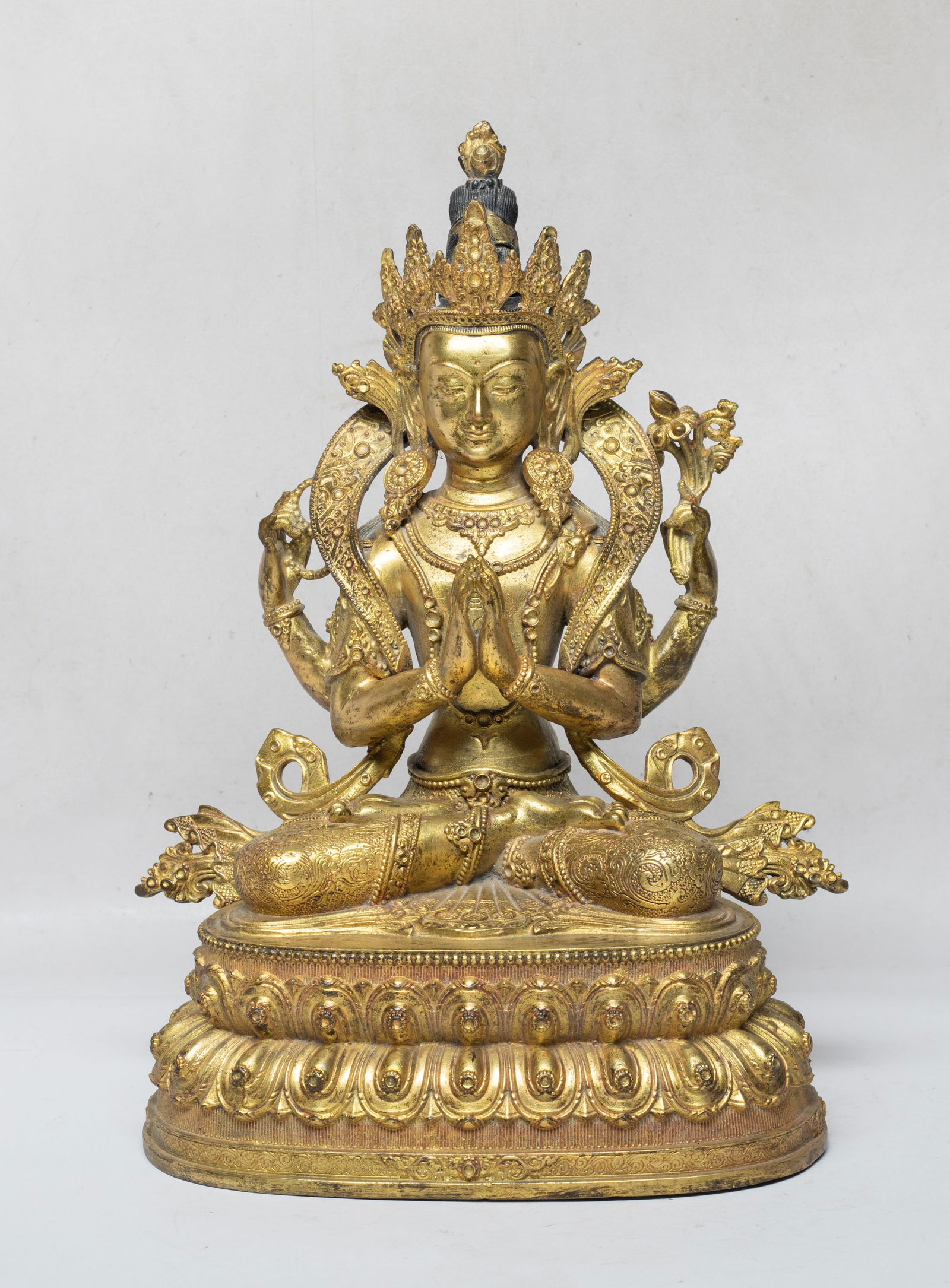 Large Chinese Gilt Bronze Sculpture of Buddha: The Buddha cast seated on a waisted lotus throne, the front pair of hands in namaskara mudra and the rear hands holding attributes, wearing a long curled scarf and a dhoti, decorated with elaborated d