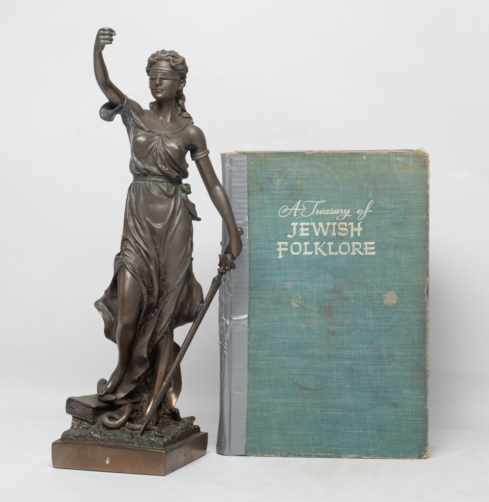 Vintage Book, Table Sculpture: The table sculpture molded as a standing woman holding a sword in left hand, her right foot stepping on a snake and a book, and a vintage book titled A Treasury of Jewish Folklore. Approx. 11.5*4.5*3.