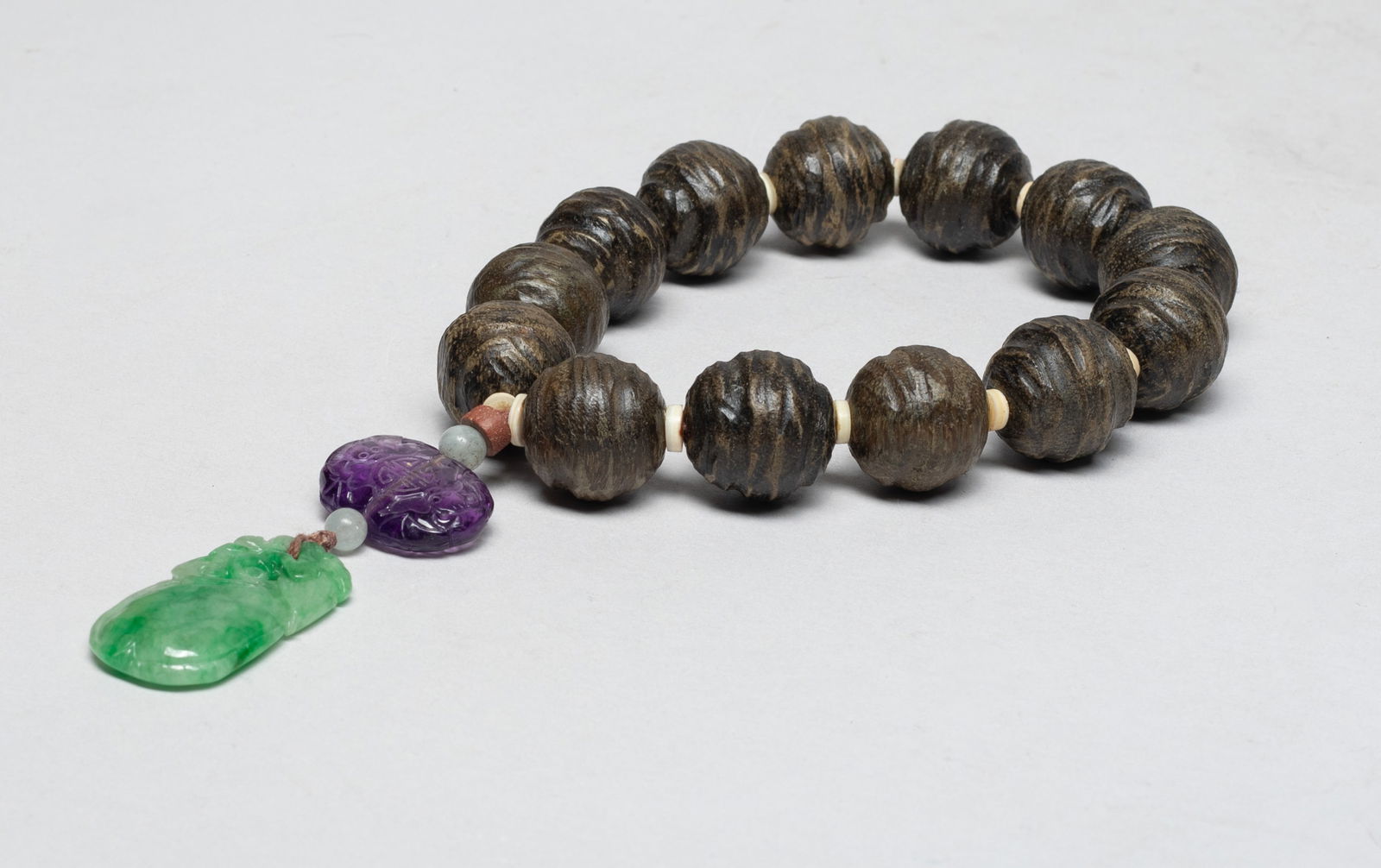 Estate Chinese Agarwood, Jade Prayer Beads: A string of Chinese agarwood carved prayer beads, with a purple stone bead carved with bats and shou characters, and a jade pendant carved with bat and fruit. Approx. 0.7 inch D (wood bead size), 60 g