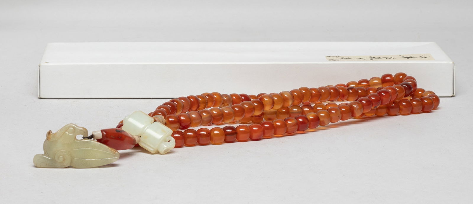 Long Chinese Cameo Agate, Jade Prayer Beads: A long string of Chinese cameo agate prayer beads, suspended with a white and russet jade pendant, a large agate bead, and a russet jade pendant of bird form, with box. Approx. 35 inch L (string size)