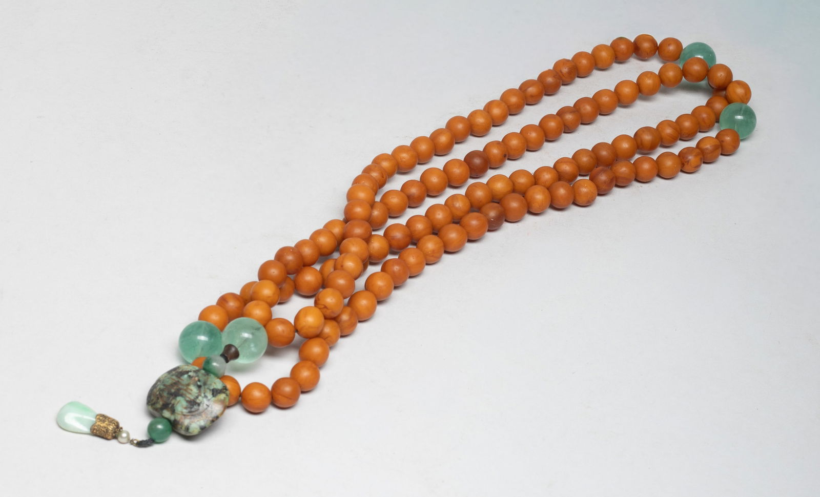 Chinese Amber, Stone Prayer Beads: A long string of Chinese amber and stone carved prayer beads, with two stone pendants. Approx. 56 inch L. The Estate of S Pasadena, CA, 2023.