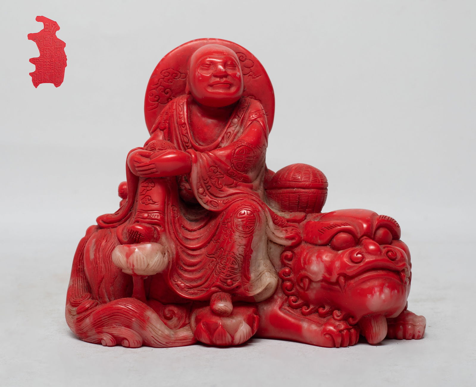 Chinese Export Stone Sculpture of Luohan: The Luohan carved seated on the recumbent beast, his feet stepping on lotus, wearing a long flowing robe inscribed with shou characters and clouds, the beast back supporting books and a box. Approx. 4