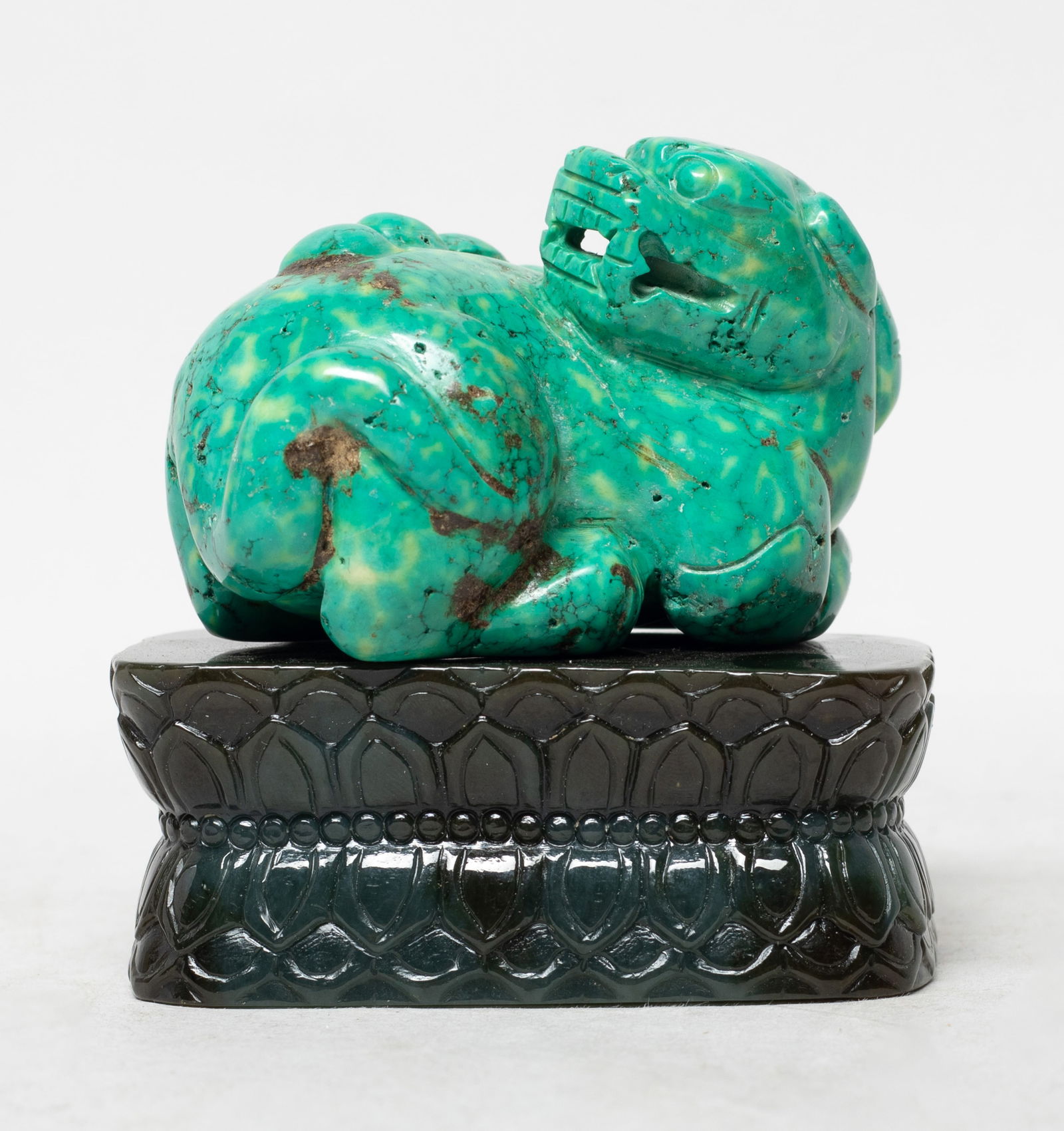 Chinese Stone Sculpture on Jade Base: Carved as a recumbent beast with its head turned backwards, its four legs tucked under its body, with raised boss shaped spine, the jade base carved with overlapping lotus petals. Approx. 2.7*1.8*1.8