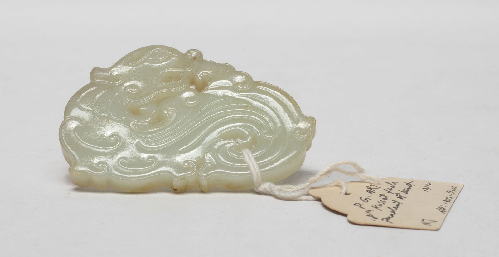 Chinese Russet Jade Pendant: Finely carved and reticulated as a recumbent mythical beast, its head turned backward, the face rendered with elongated eyes, its head flanked by pointed ears, the body detailed with scrolls, the ston