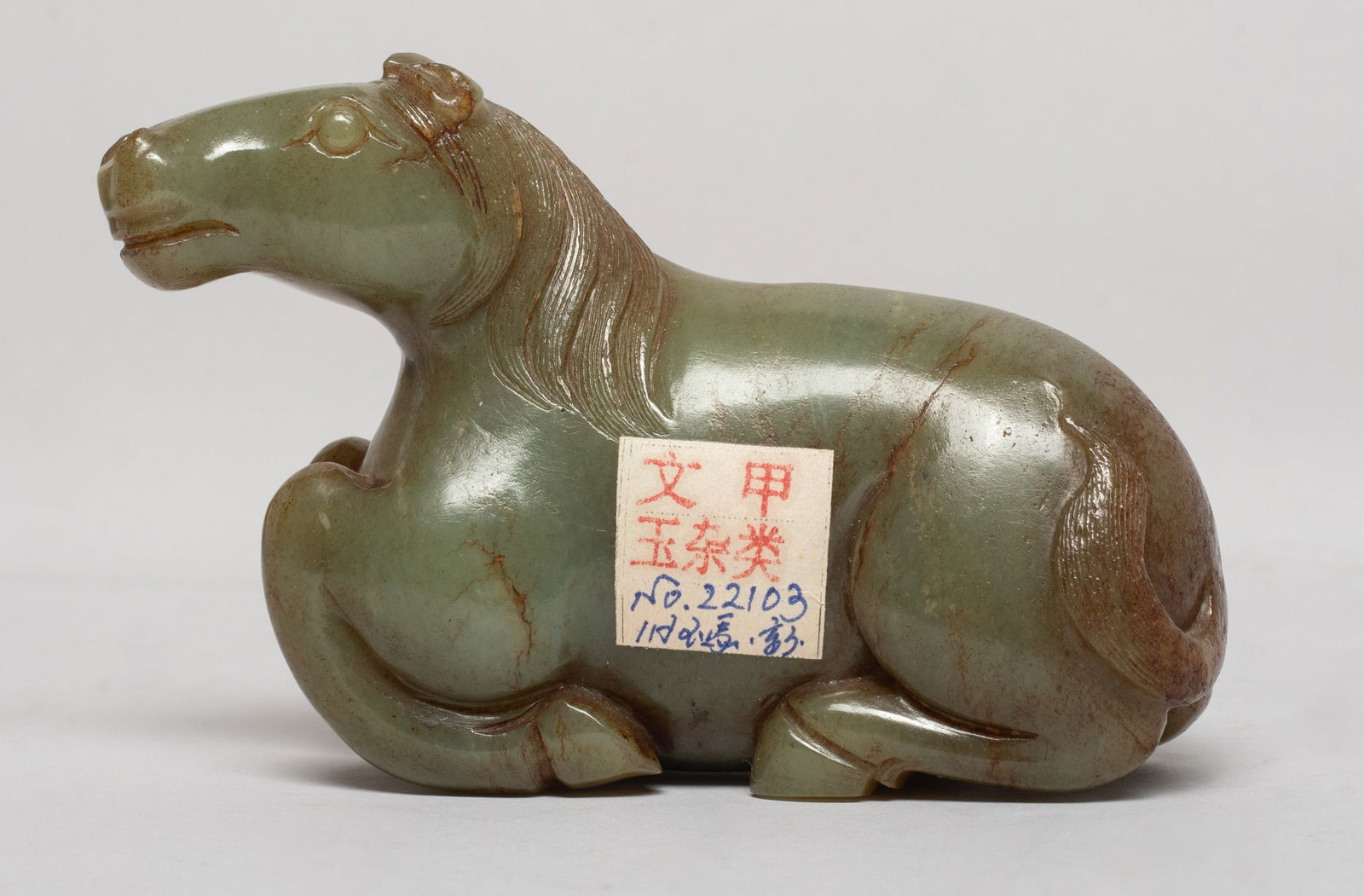 Chinese Russet Jade Sculpture of Horse: The powerful recumbent animal carved with its head turned slightly to the left, the head with flared nostrils and bulging eyes, below the ears and flowing incised mane, the tail resting along the left
