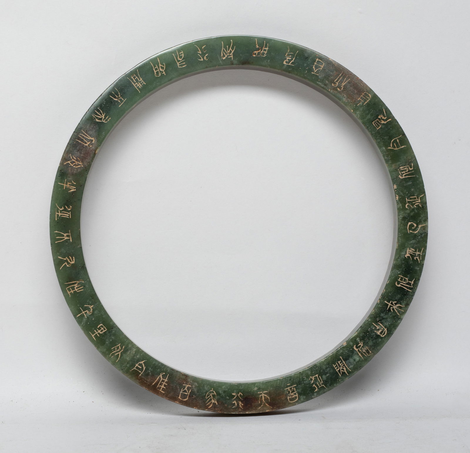 Large Chinese Jade Carved Huan: The large spinach green and russet jade huan incised with characters on the top and bottom, the sides with a band of scrolls. Approx. 7 inch outer diameter, 5.8 inch inner diameter. The Estate of the