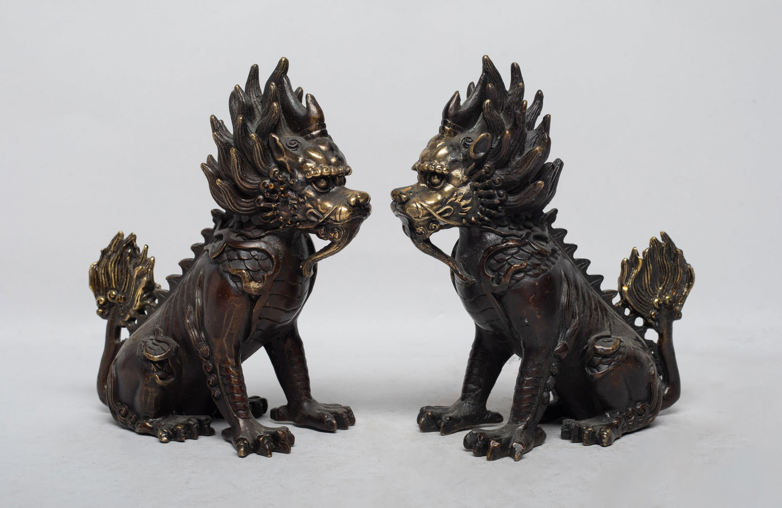 Two Chinese Bronze Sculptures of Qilin: The horned and scaled mythical beast cast in crouching pose, with flaming mane and ample tail feathers, the face with bulging eyes and wide nostril. Approx. 5.7*5.4*2.8 inch (each). The Estate of the