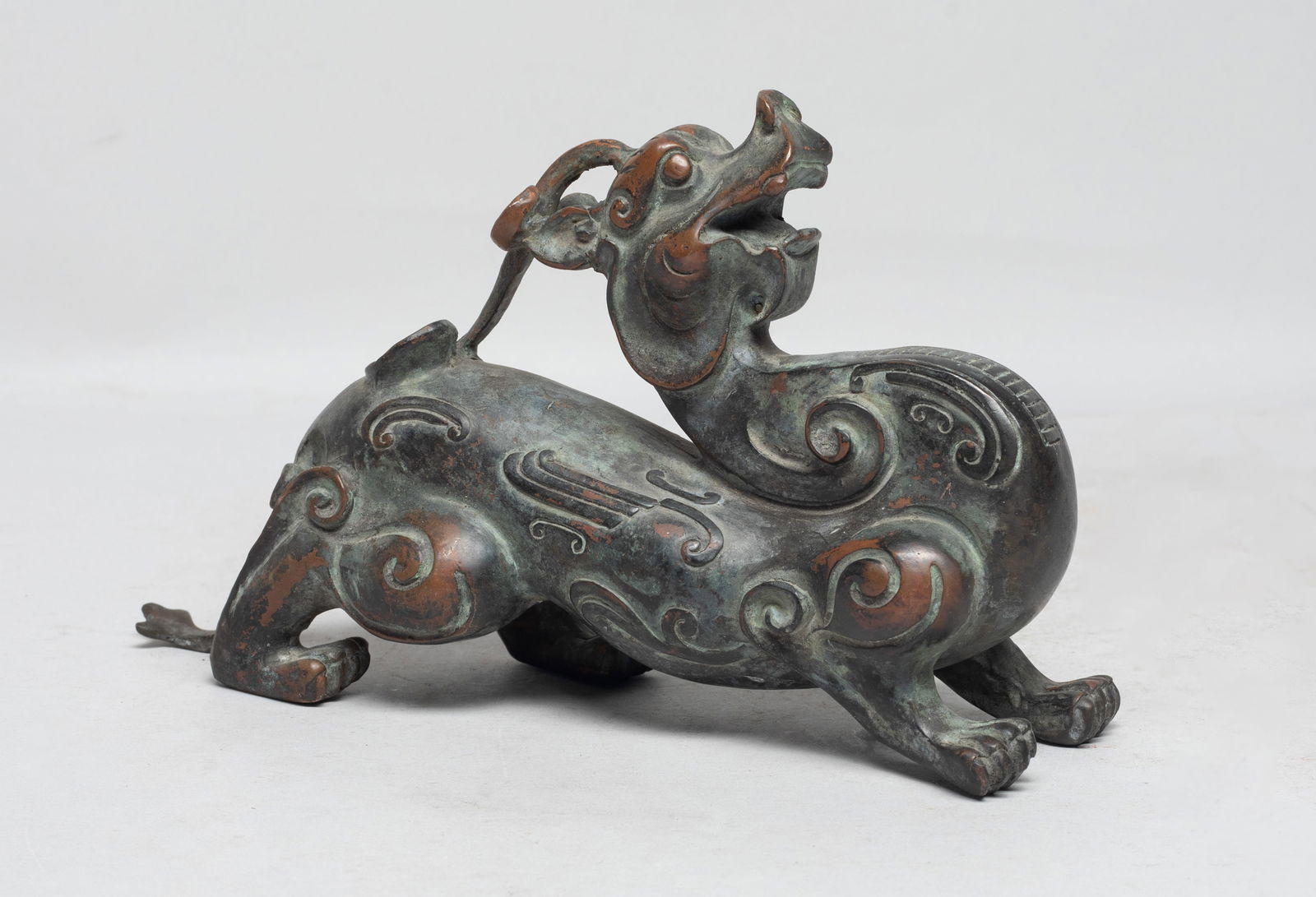 Chinese Bronze Sculpture of Beast: The horned mythical beast naturalistically cast with bulging eyes and agape mouth, the neck bent backward and the head graciously looking upward, encircled by scrolls to the thighs and shoulders.