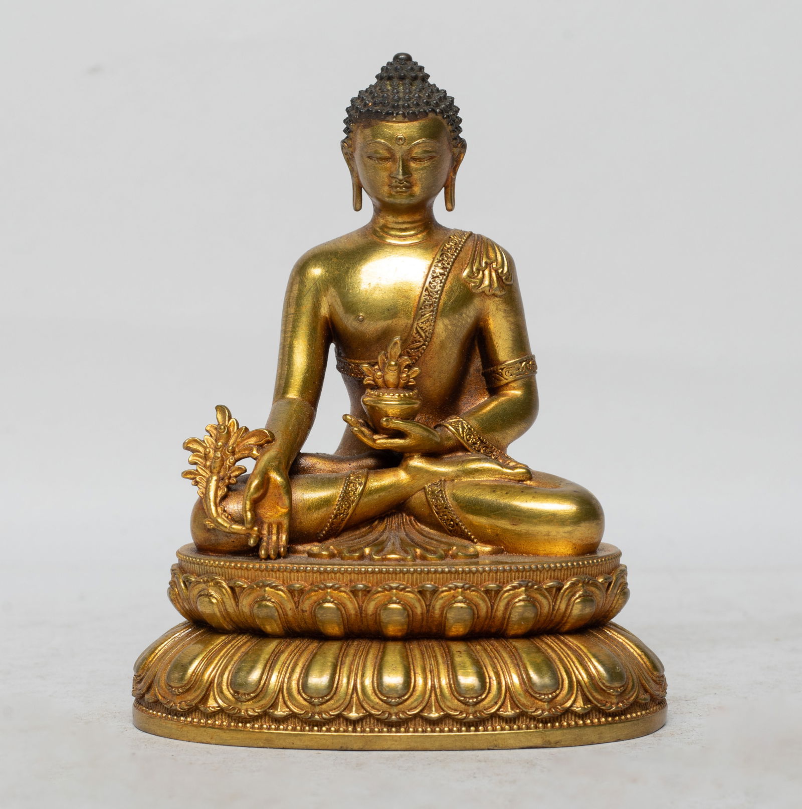 Chinese Gold on Bronze Sculpture of Buddha: The Buddha cast seated on a double layered lotus base, the left hand holding a bowl and right hand holding flower, the face with serene expression. Approx. 4.1*3.1*2.2 inch. The Estate of the Store Cl