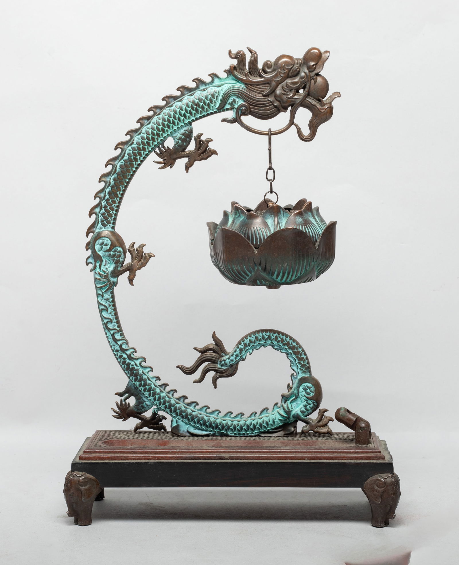 Fine Chinese Bronze Dragon Hanging Censer: Cast as a C-shaped dragon with its mouth agape carrying a ball, suspending a lotus form censer under the chin, with a rectangular base. Approx. 11.7*8.2*3.3 inch. The Estate of Los Angeles. CA. 2024.