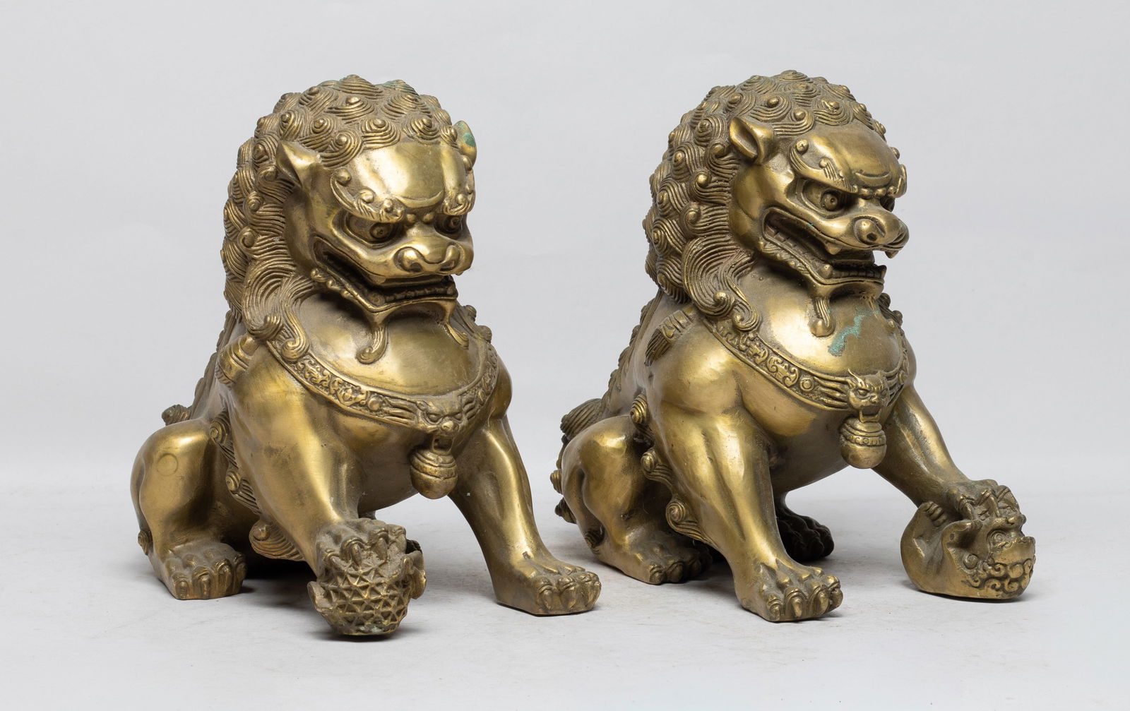 Two Chinese Export Brass Sculptures: Two Chinese brass table sculptures cast of crouching foo dog form, one beast carrying a ball in right paw, the other carrying a cub in left paw. Approx. 7.7*7.7*4.5 inch (each). The Estate of the E Lo