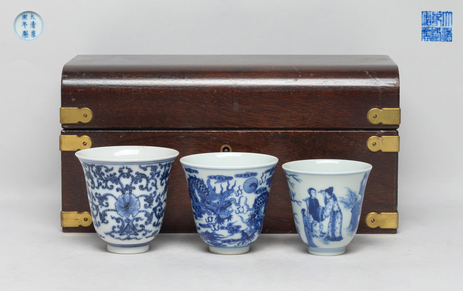 Set Chinese Blue & White Porcelain Tea Cups: Three blue and white porcelain tea cups, one painted with figural scene, one with dragons pursuing a flaming pearl amidst clouds, the other with lotus foliage, bats and fish, each bottom with a six-ch