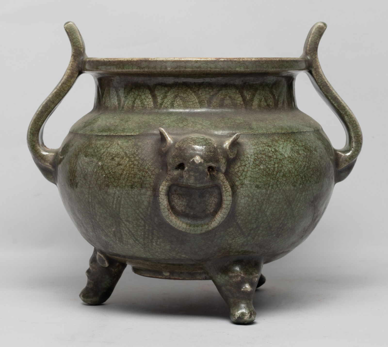 Large Chinese Longquan Porcelain Censer: The compressed ovoid body with a short neck and dished rim, flanked by two scroll handles and two faux-ring beast masks, all supported on three mask-to-paw feet, the exterior carved in low relief with
