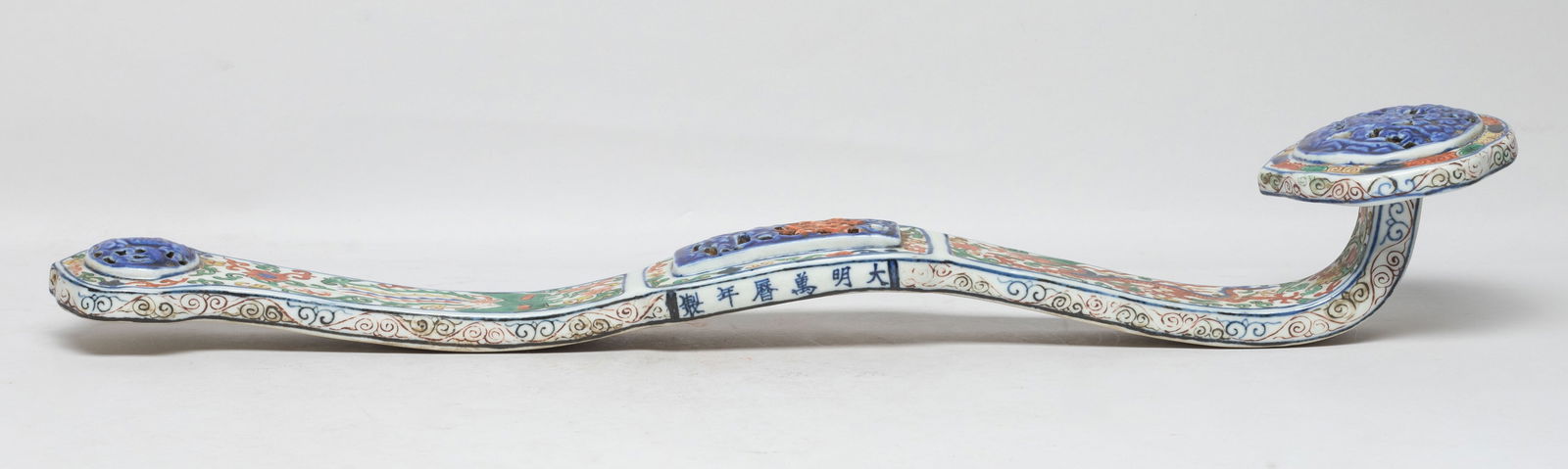 Chinese Porcelain Sculpture of Ruyi: The ruyi head carved in openwork with intertwined flower branches, the centre with Chinese know and clouds, the terminal with a bat, the arched shaft painted with dragon and phoenix amidst lotus folia