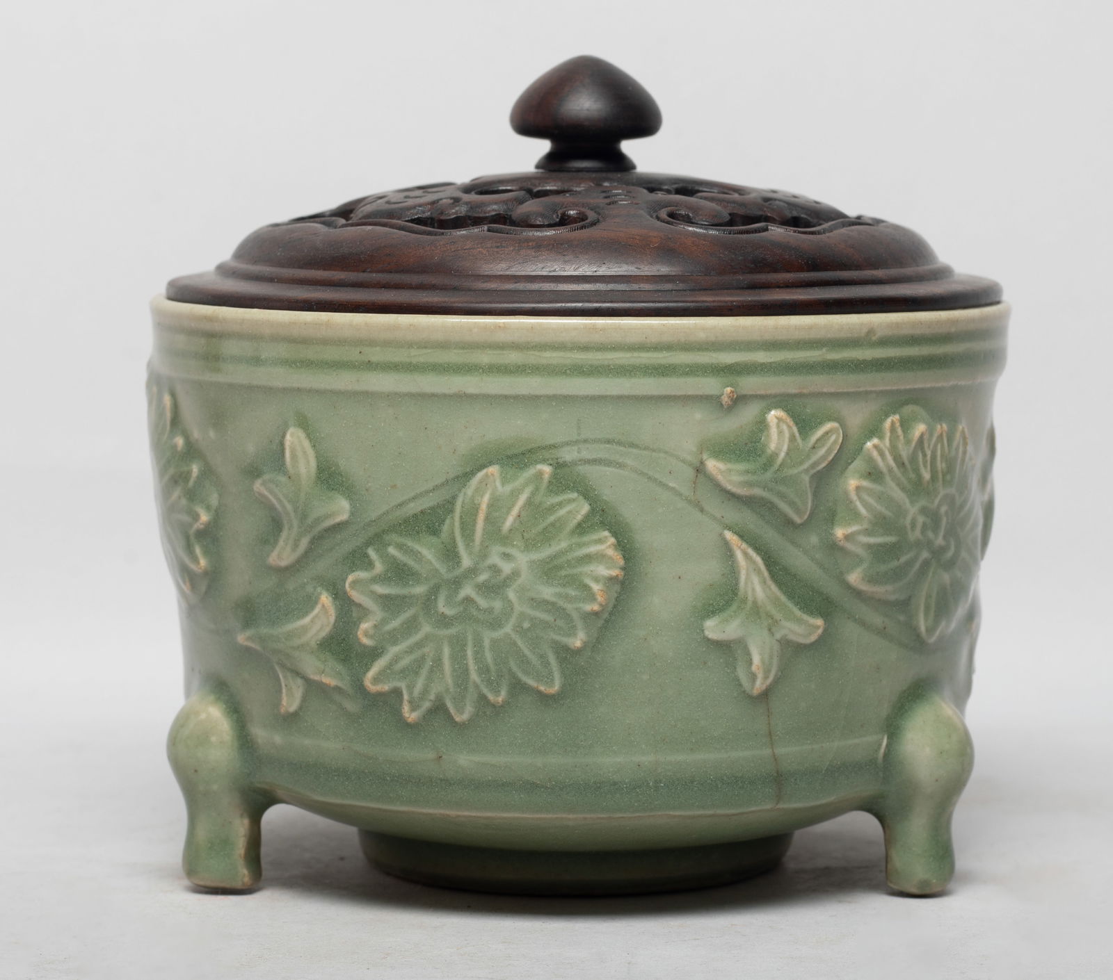 Chinese Longquan Porcelain Censer w/ Cover: Of cylindrical form with three short cabriole legs, the exterior carved with meandering lotus sprays, applied on the exterior and interior sides with crackled celadon glaze, with an openwork wood cove