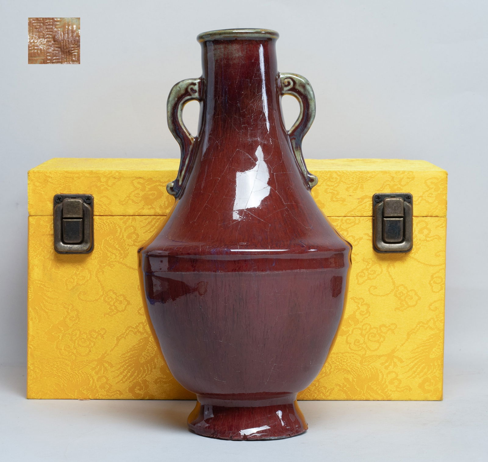 Chinese Flambe Glazed Porcelain Vase: The ovoid body rising from a splayed foot to an angled shoulder and a columnar neck with two handles, the exterior covered in crackled red glaze with lavender blue streaks, the bottom incised with a s