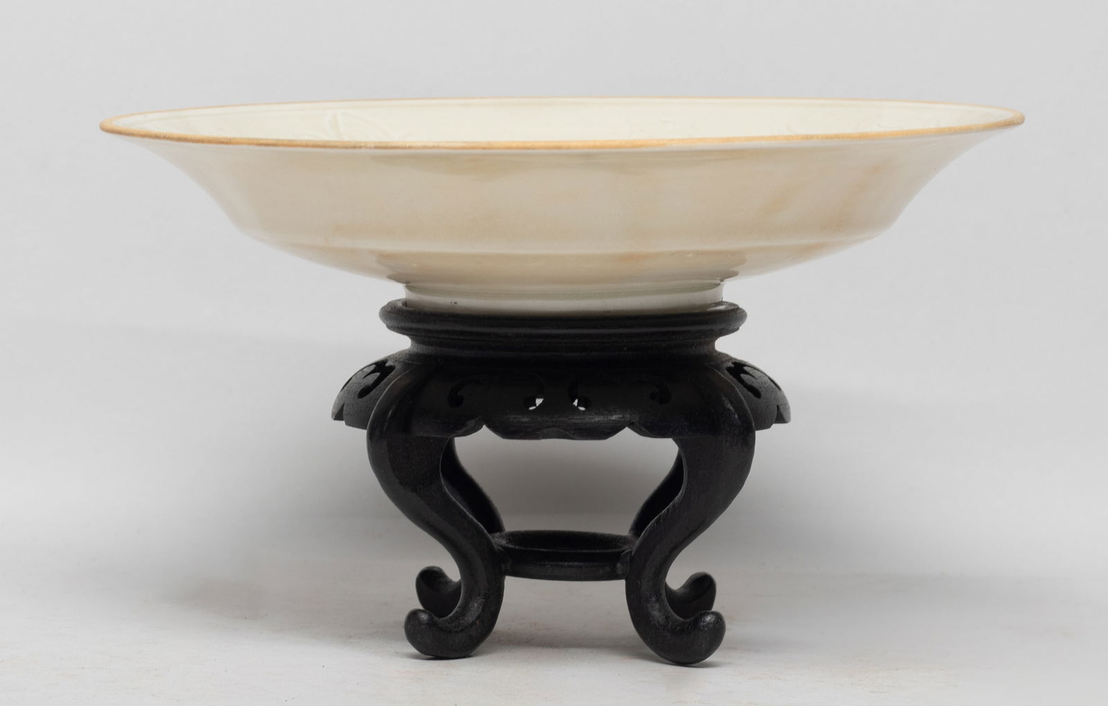 Chinese Ding Ware Porcelain Deep Plate: The plate interior carved in low relief with a dragon sinuous amdist lotus, overall covered in creamy glaze, affixed to a tall wood stand. Approx. 4.3*7.3 inch (w/ stand). The Estate of the Miura, Ven