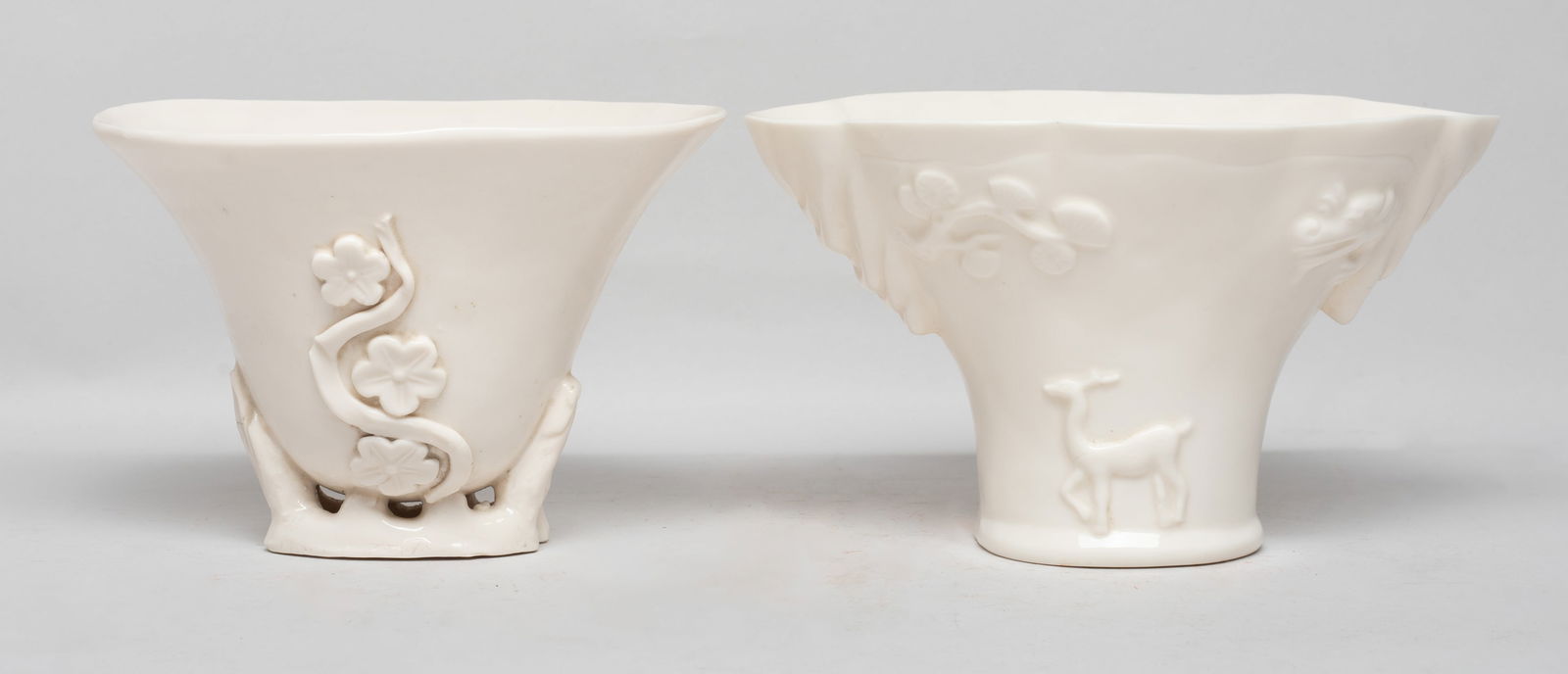 Chinese Blanc De Porcelain Cups: One cup carved with deer, dragon and pine tree branch, the reverse with bear, crane and plum blossoms, the other cup carved with bamboo and plum blossoms forming the base, both covered with creamy gla