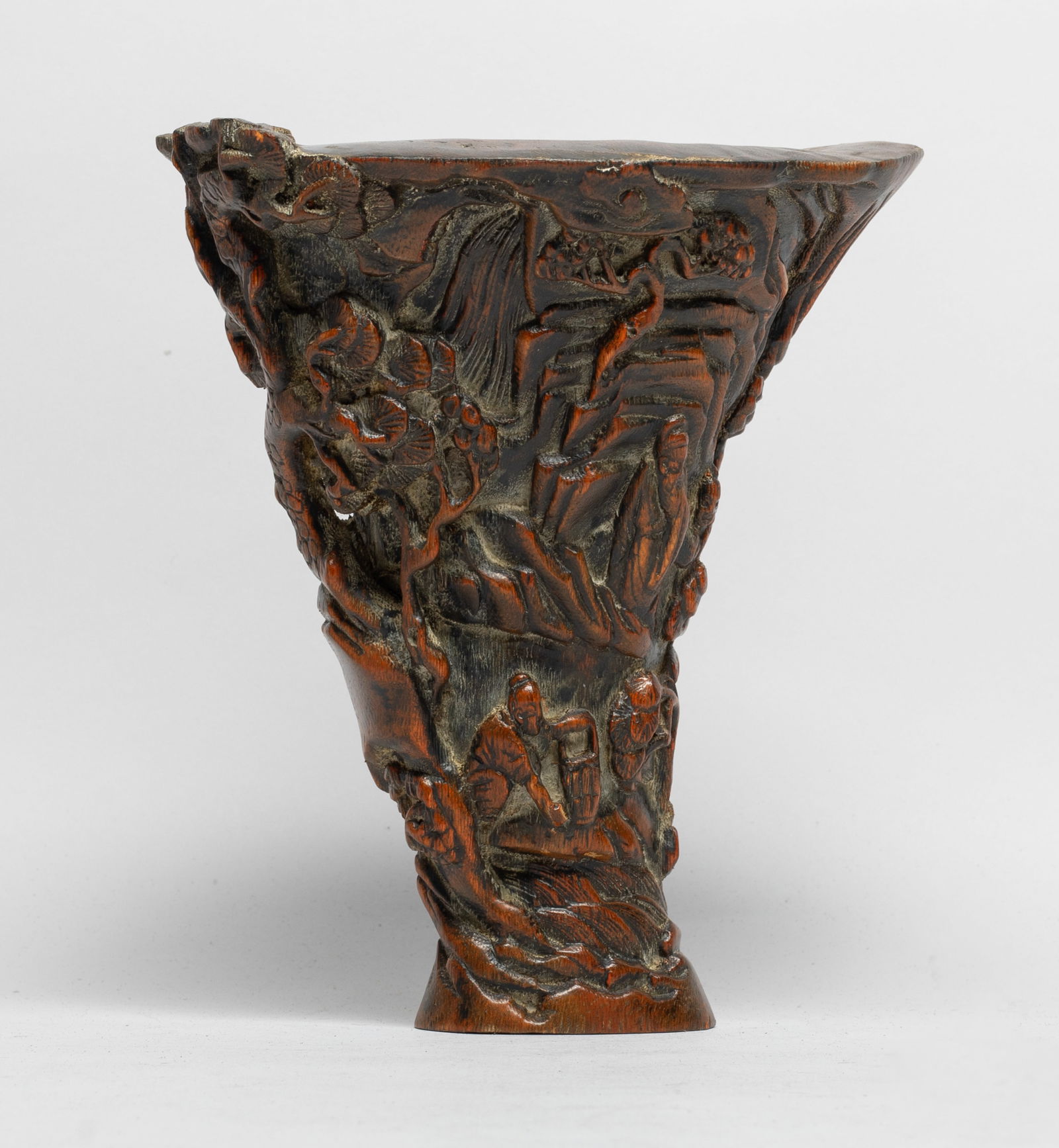 Chinese Bark of Agarwood Libation Cup: The flared cup finely carved in relief with scholars and their servants in various activities, all in a mountainous landscape strewn with pine tree forming the handle as well as wutong amidst streams