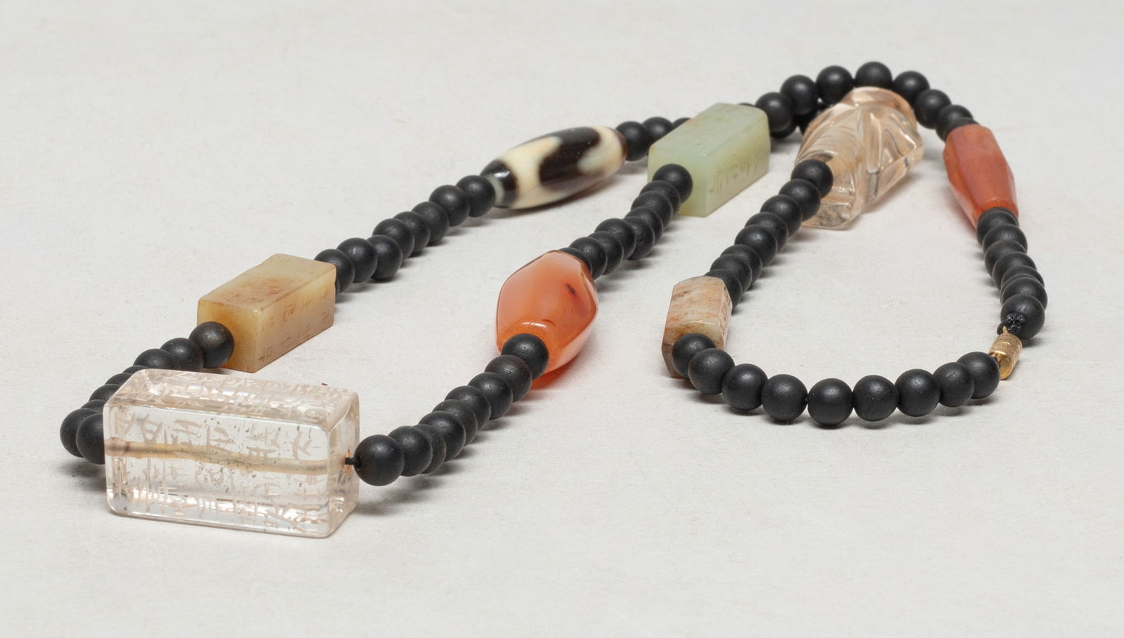 Chinese Export Agarwood, Jade, Stone Necklace: Chinese agarwood bead necklace, slightly fragrant, with two agate beads, three russet jade beads incised with characters, a crystal bead, a crystal carved figure form pendant, and a dzi bead. Approx.
