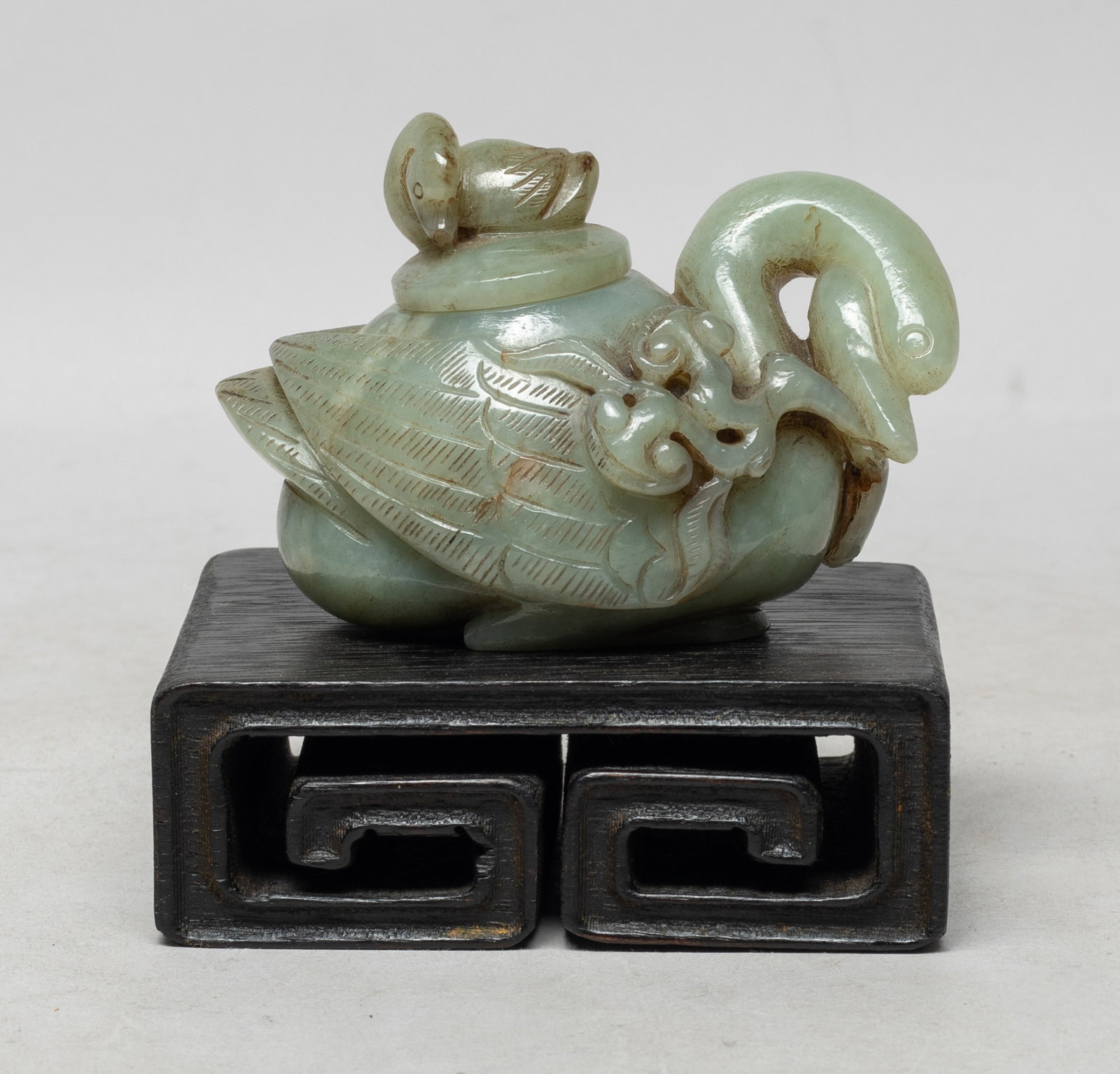 Rare Chinese Jade Pot on Wood Base: Exquisitely worked and smoothly polished in the form of a recumbent goose, its long neck extending to the head in a coiled position, its beak depicted biting on stems of lingzhi, the cover surmounted