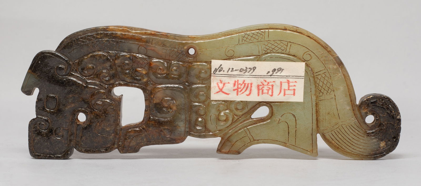 Chinese Export Russet Jade Pendant: The flat stone cut and worked in the form of a stylised dragon in profile, its body incised with archaic scrolls terminating in a curled tail, perforated with apertures at mouth and back. Approx. 5.4*