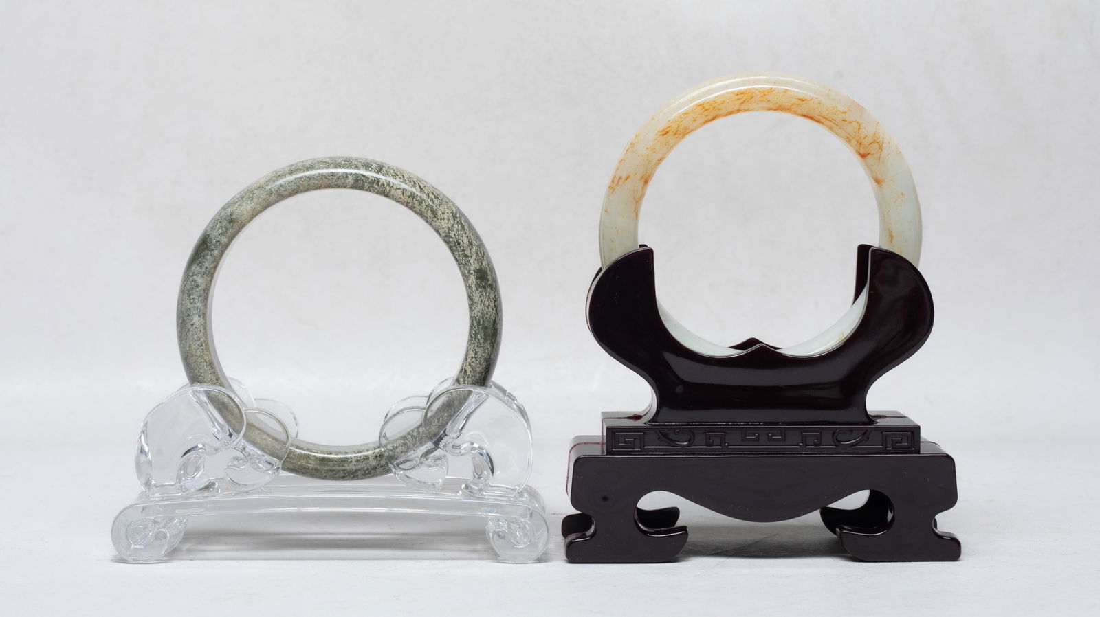 Two Chinese Jade/ Hard Stone Bangles: Two Chinese jade / hand stone carved bangles, each with a matched stand. Approx. 3 inch outer diameter, 2.4 inch inner diameter (larger bangle).