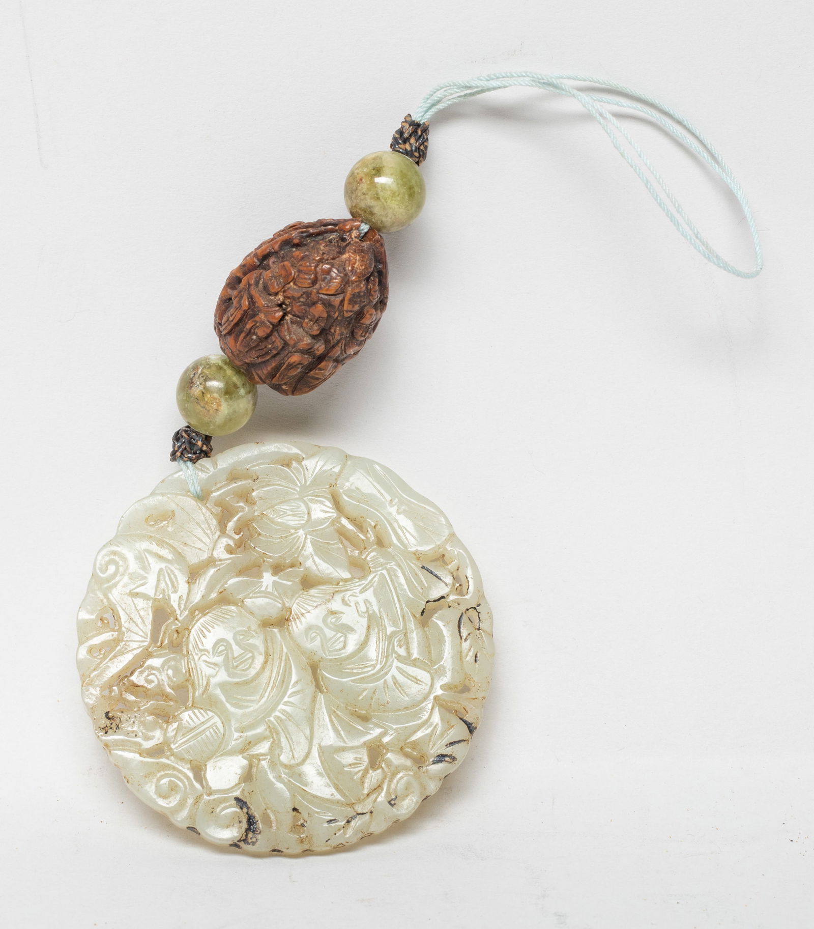 Chinese Jade Pendant w/ Carved Nut Bead: The jade pendant of circular shape, carved in openwork with Hehe Erxian, bat and lingzhi, one figure holding lotus and the other holding a box, with two gemstone beads and a nut bead carved Luohan. Ap