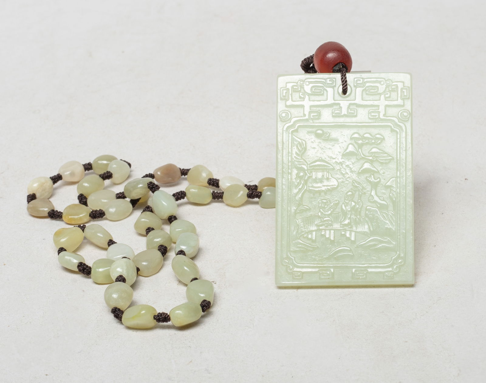 Chinese Export Jade Necklace w/ Pendant: Long Chinese jade bead necklace, suspended with an agate bead and a pale celadon jade plaque of rectangular shape, one side carved with a scholar and a boy walking on a bridge in landscape setting, th
