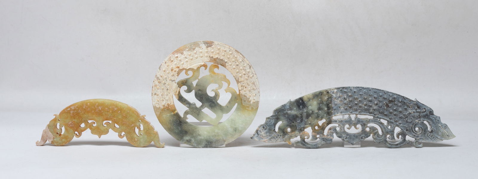 Set Chinese Export Jade/ Stone Carvings: Set of three jade / stone carvings, one of circular huan shape reticulated with a dragon on the centre, one of elongated dragon form, the other terminating at both ends with a stylised dragon head. Ap