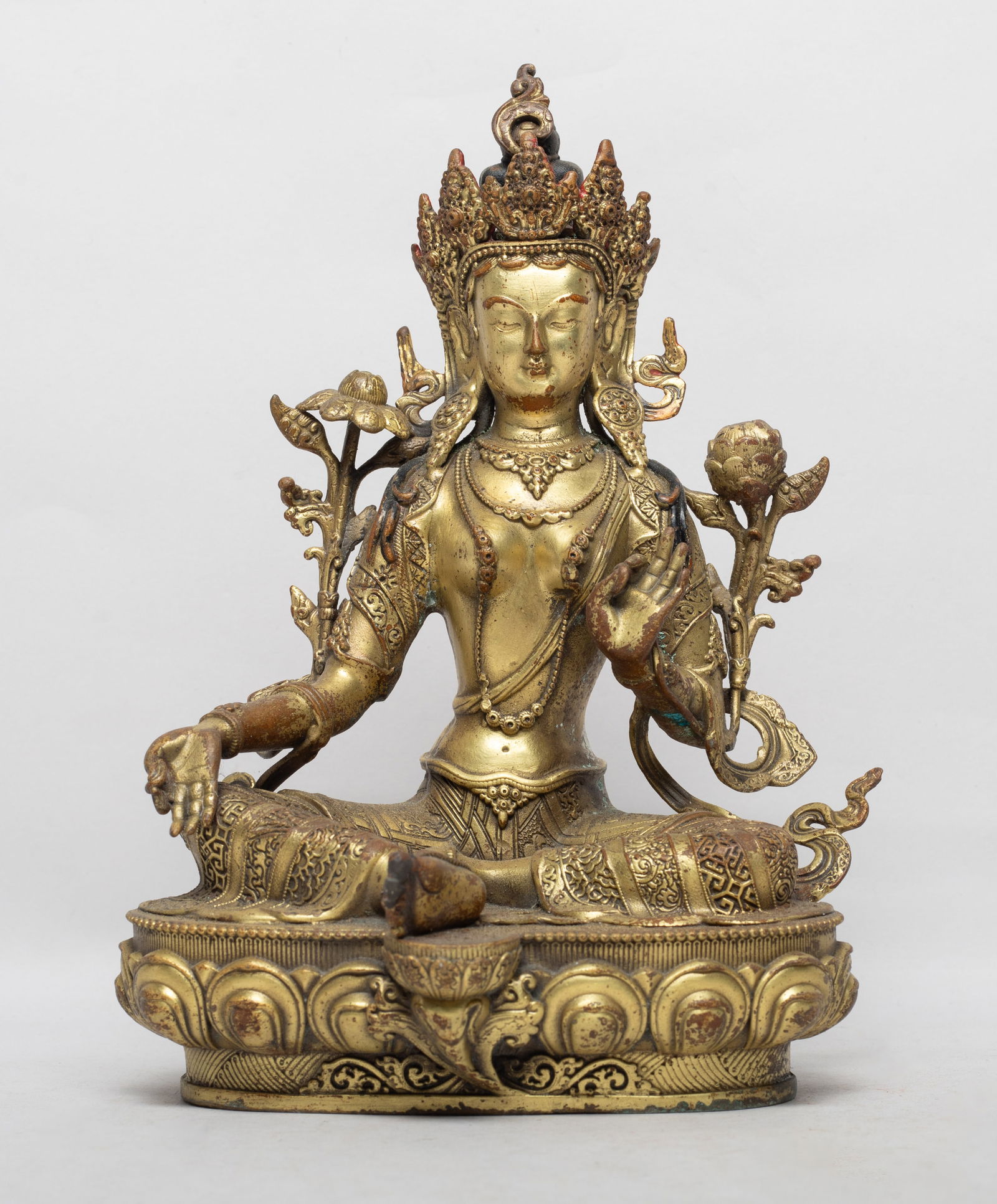 Chinese Gilt Bronze Buddha: The Buddha cast seated on a lotus base, the hands in vitarka mudra holding long stems issuing flowers, wearing delicate diadema and jewelry, the face with serene expression. Approx. 5.7*4.5*8.2 inch.